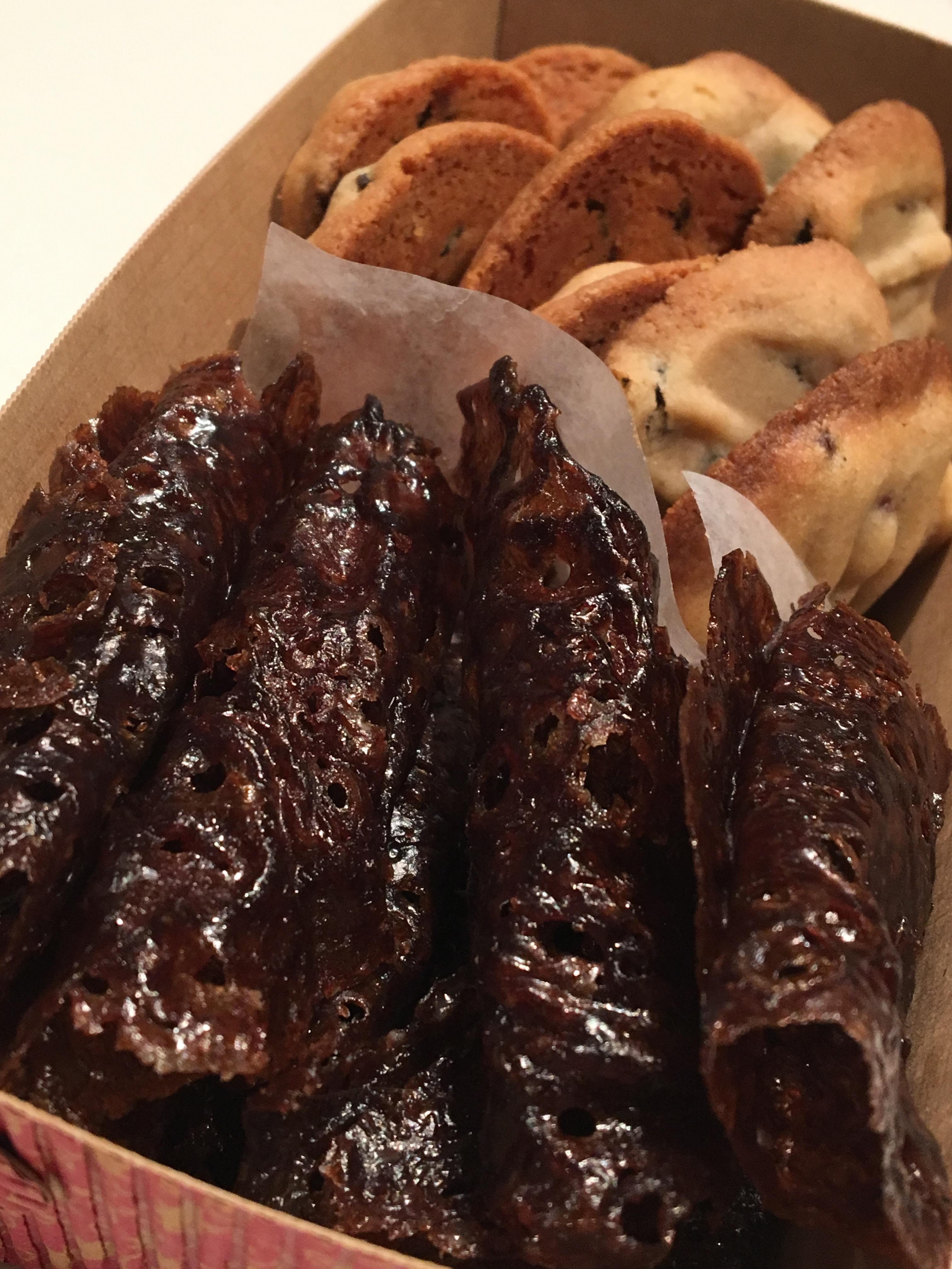 A cardboard loaf box is packed full of currant cookies and caramelized dark brown folded cookies.