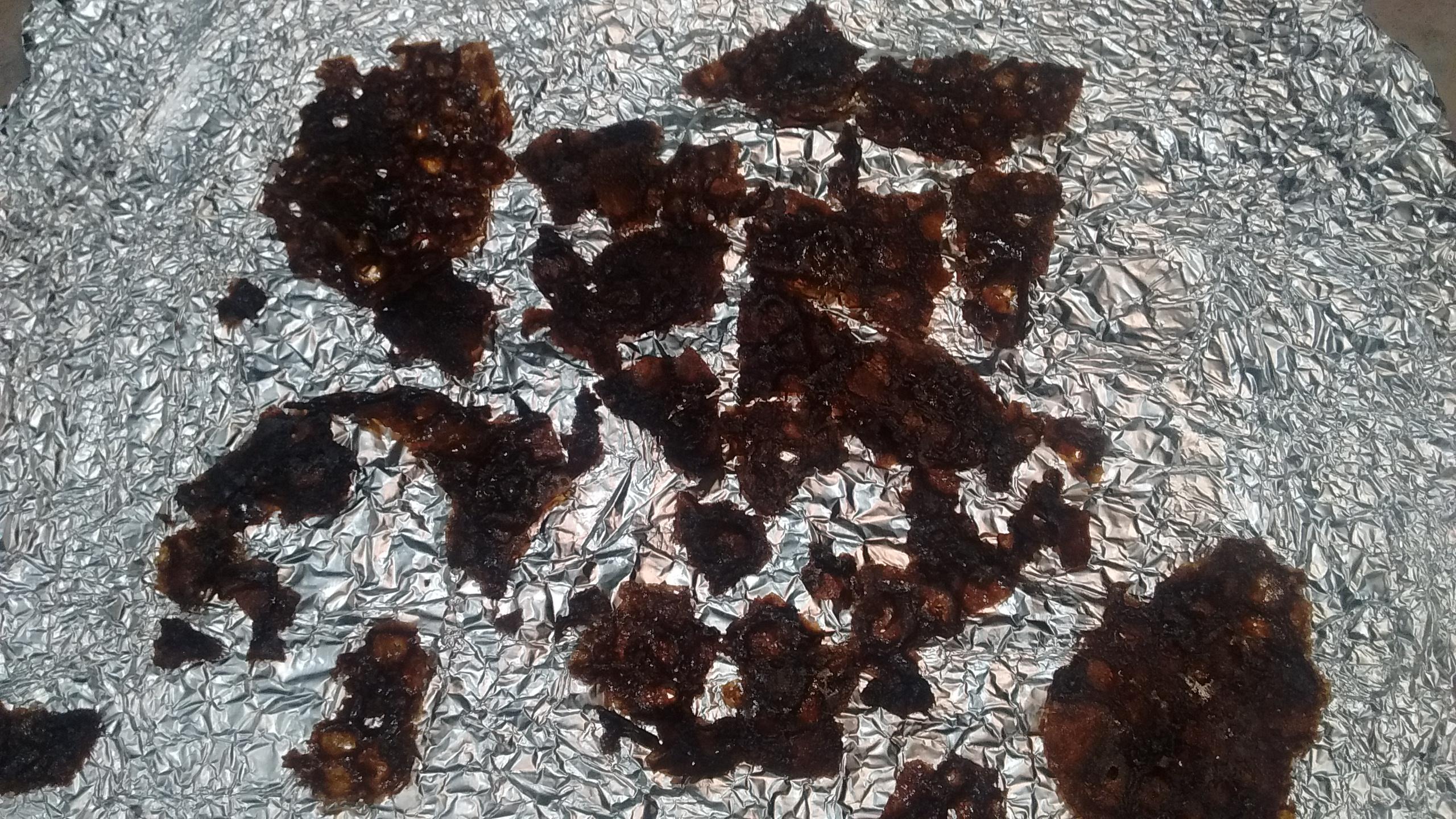 Dark brown cookie shards lie scattered on a piece of crinkled aluminum foil.