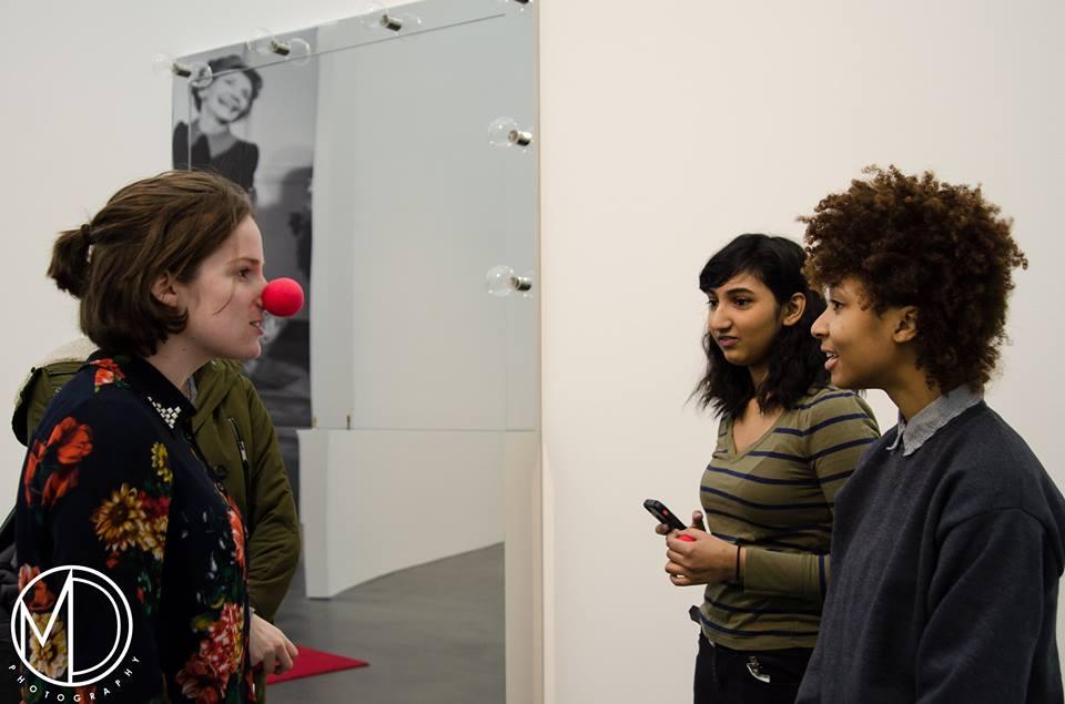 Three teenager girls stand talking together near a mirrored artwork; one wears a red Bozo-the-Clown nose. A watermark on the bottom left reads: "MD Photography."