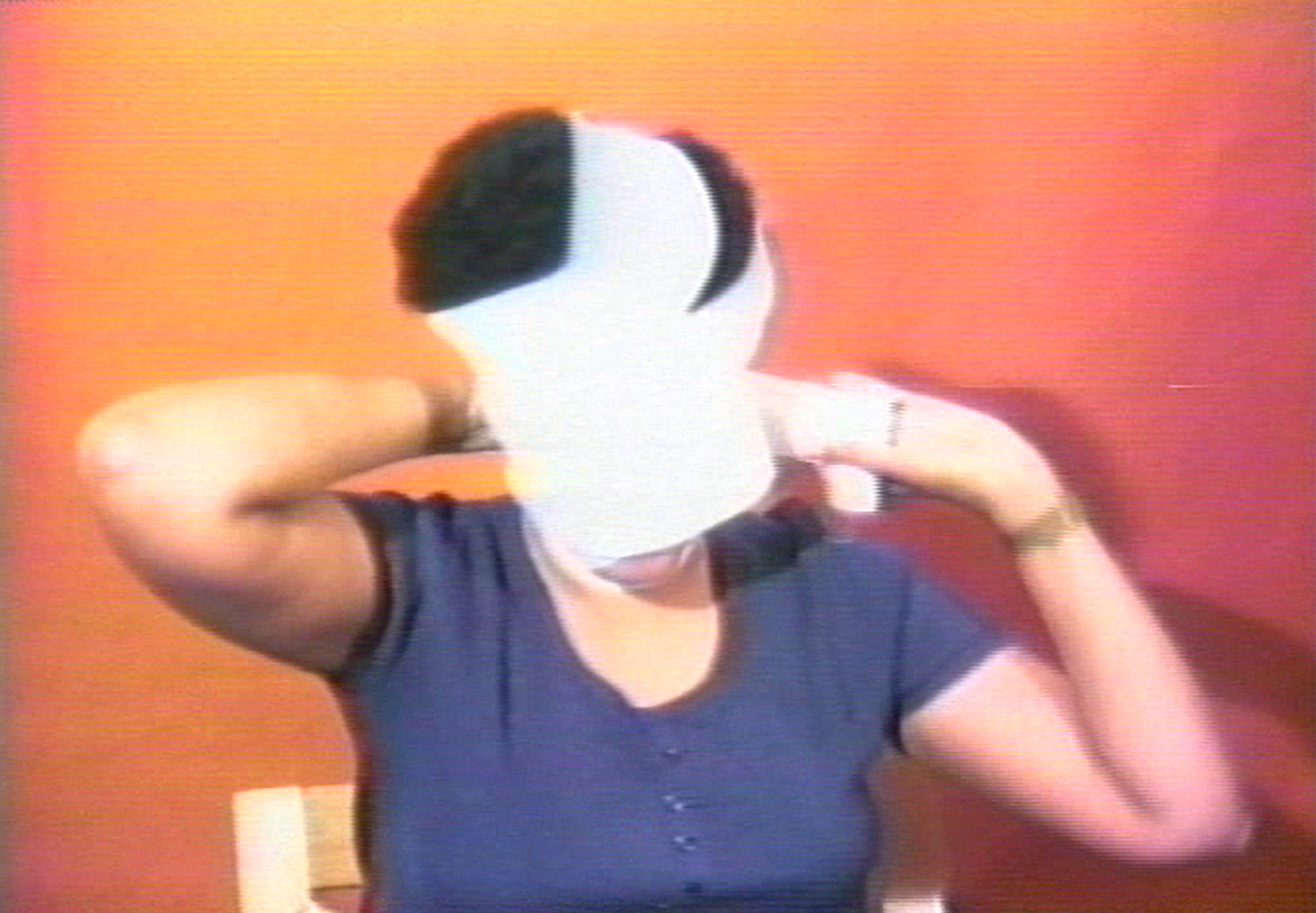 In this grainy image, a woman with a black afro is shown wrapping her face with a white bandage.