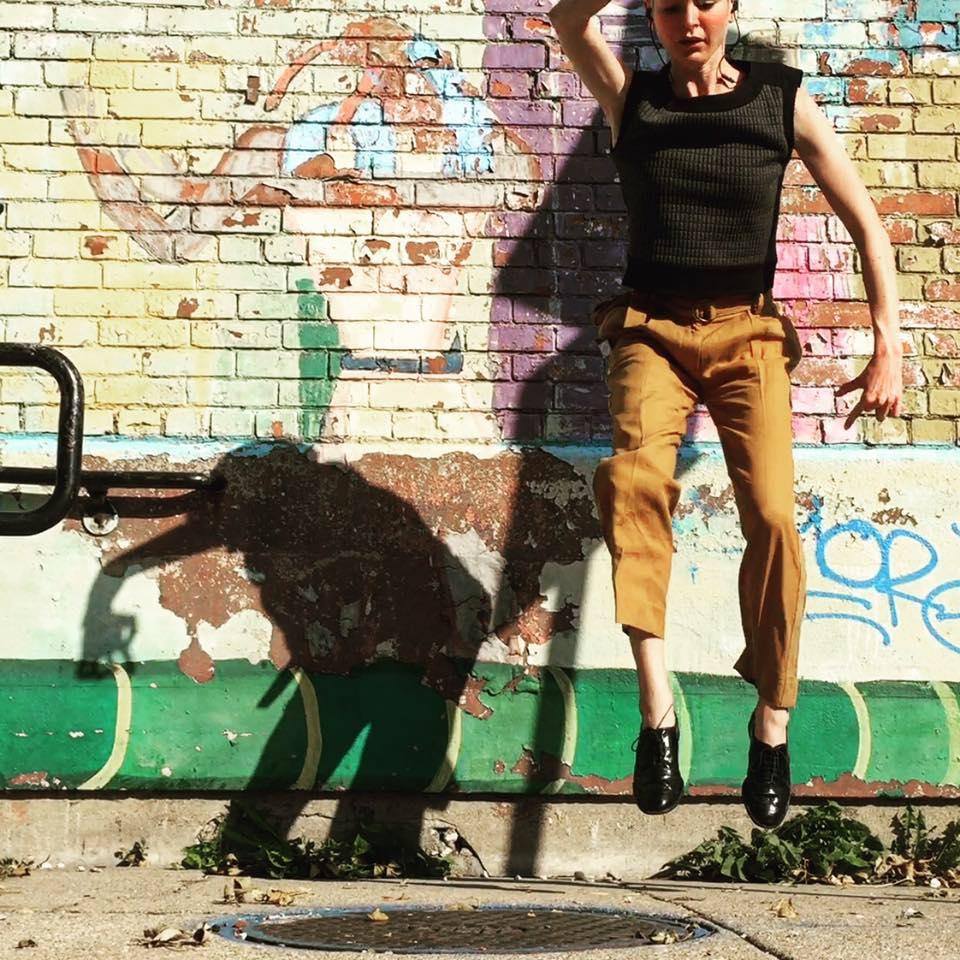 A woman is shown midjump while dancing in an urban environment.