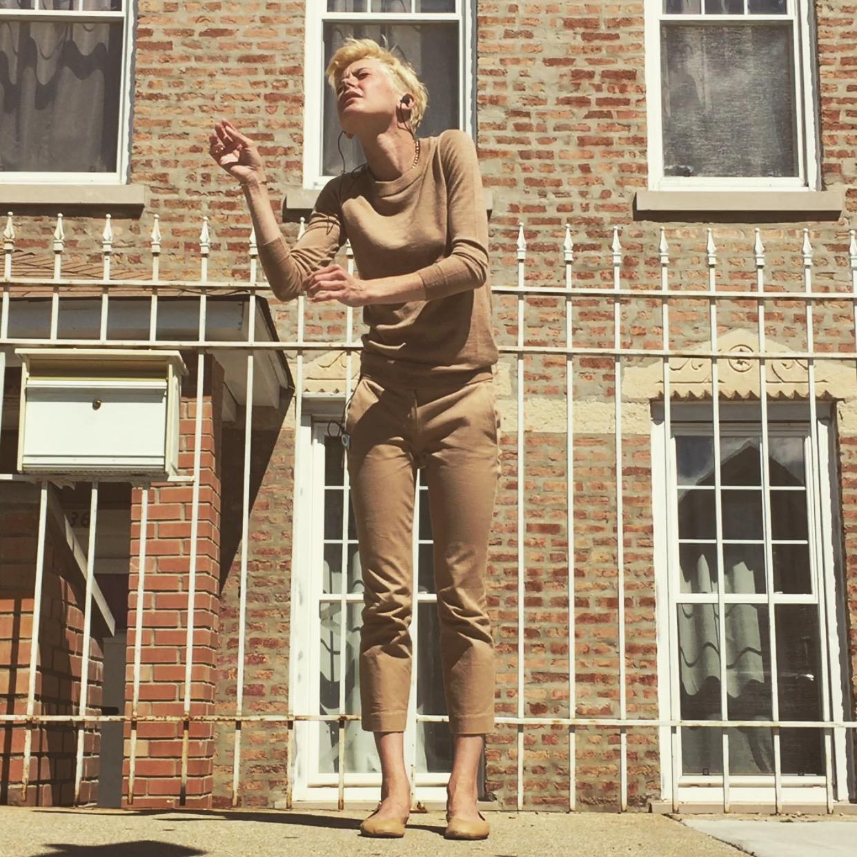 Image of a young woman dancing in front an urban-feeling apartment building.