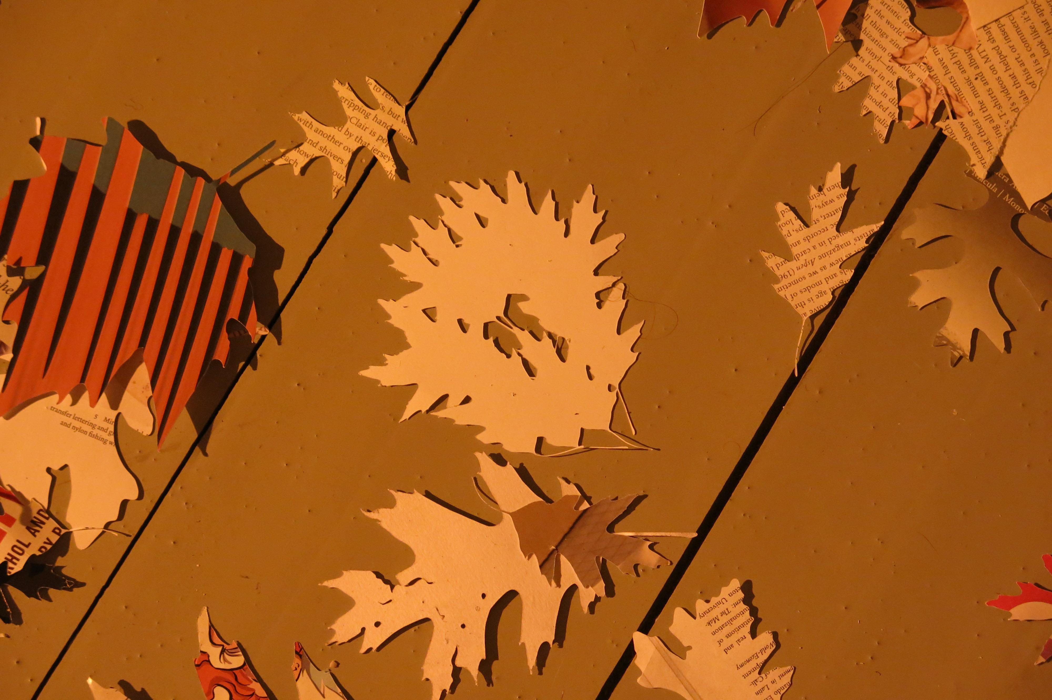 A dozen leaf shapes cut out from newspaper have been scattered on a brown background.