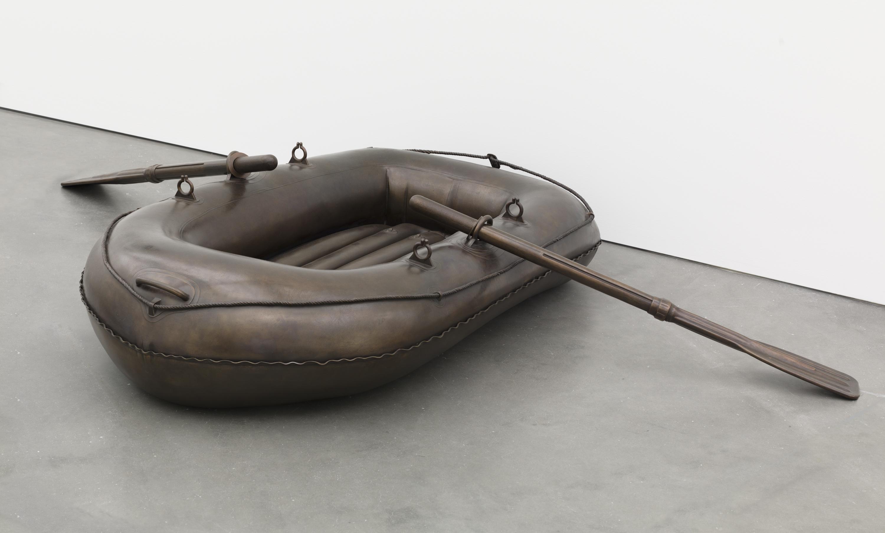 A grey-brown inflatable raft with two oars rests on a grey floor.