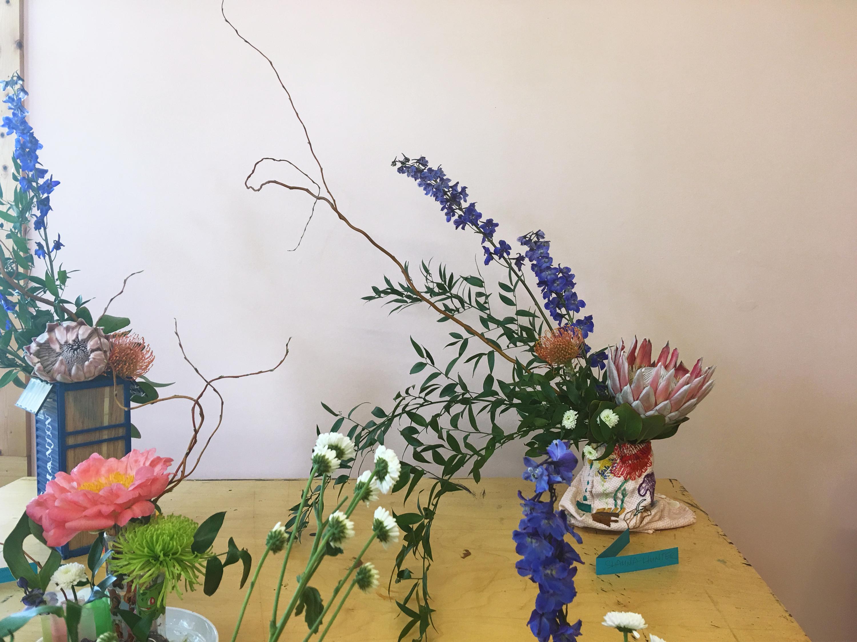 On a rough wooden table stand three small containers overflowing with flowers.