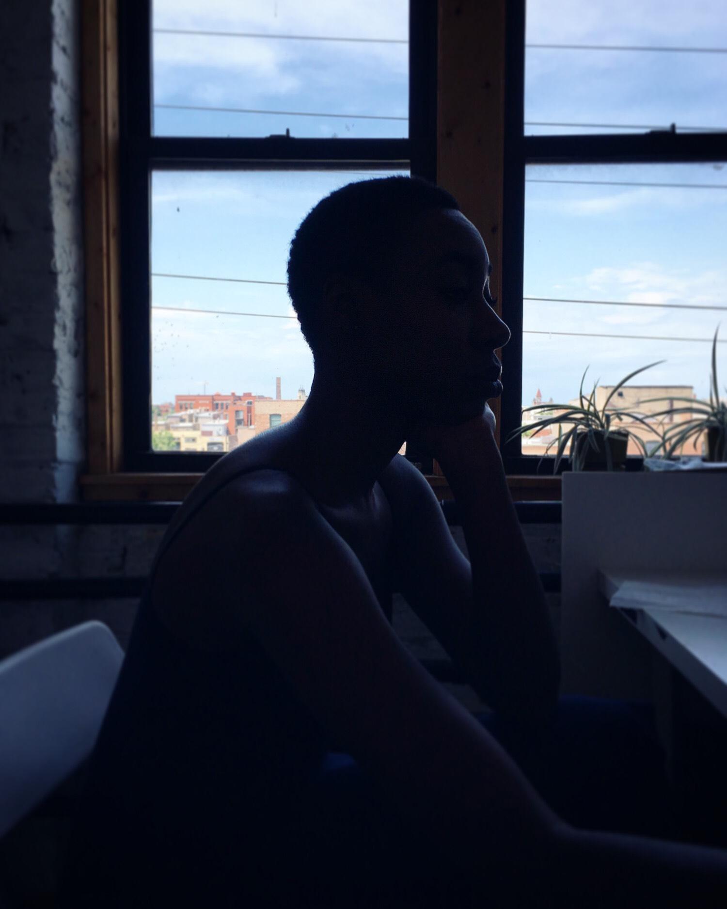 A silhouetted figure sits in front of bright windows.