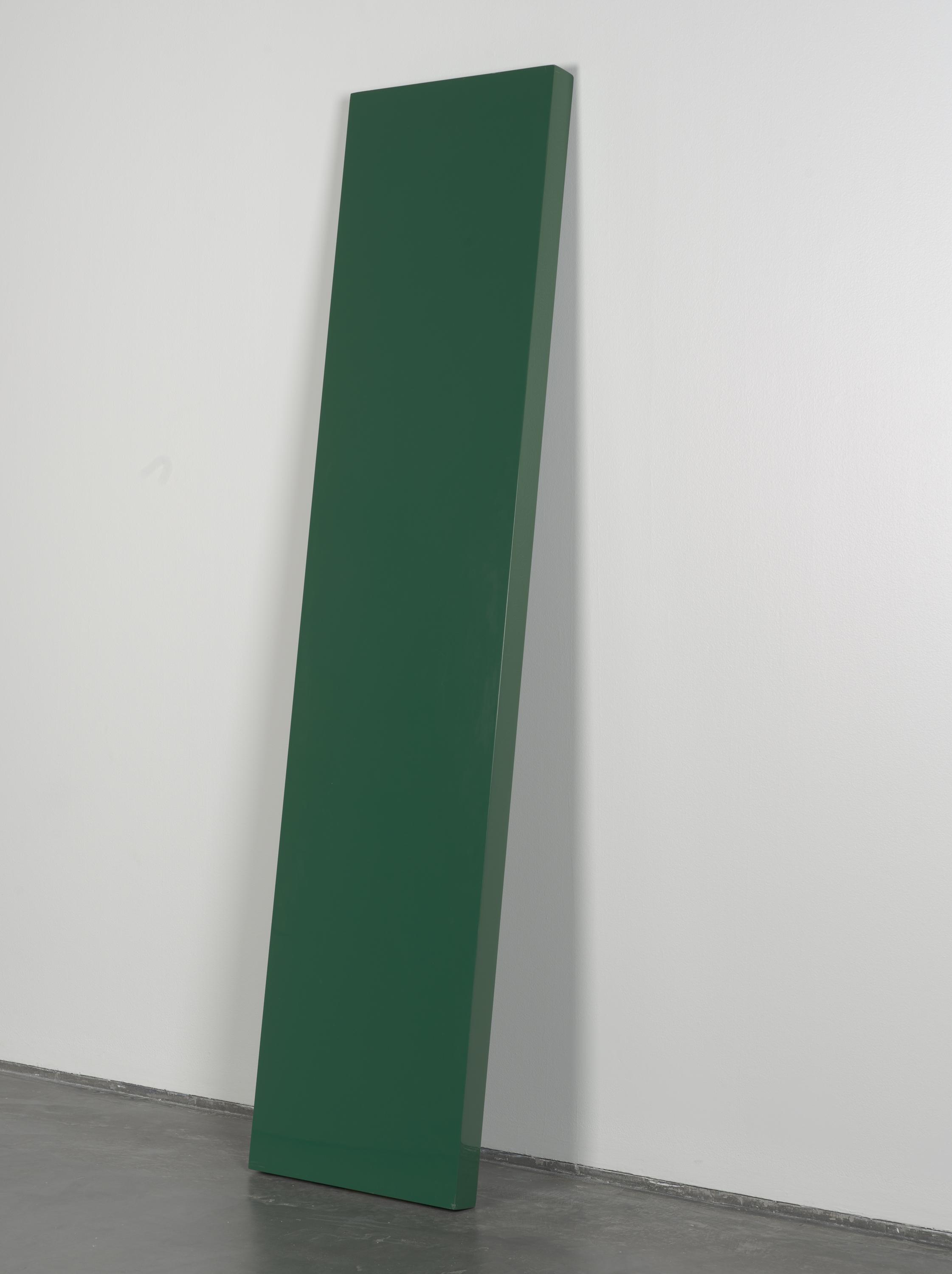 A glossy green plank leans against a white gallery wall. Its rectangular form stands vertically and would be taller than most people.