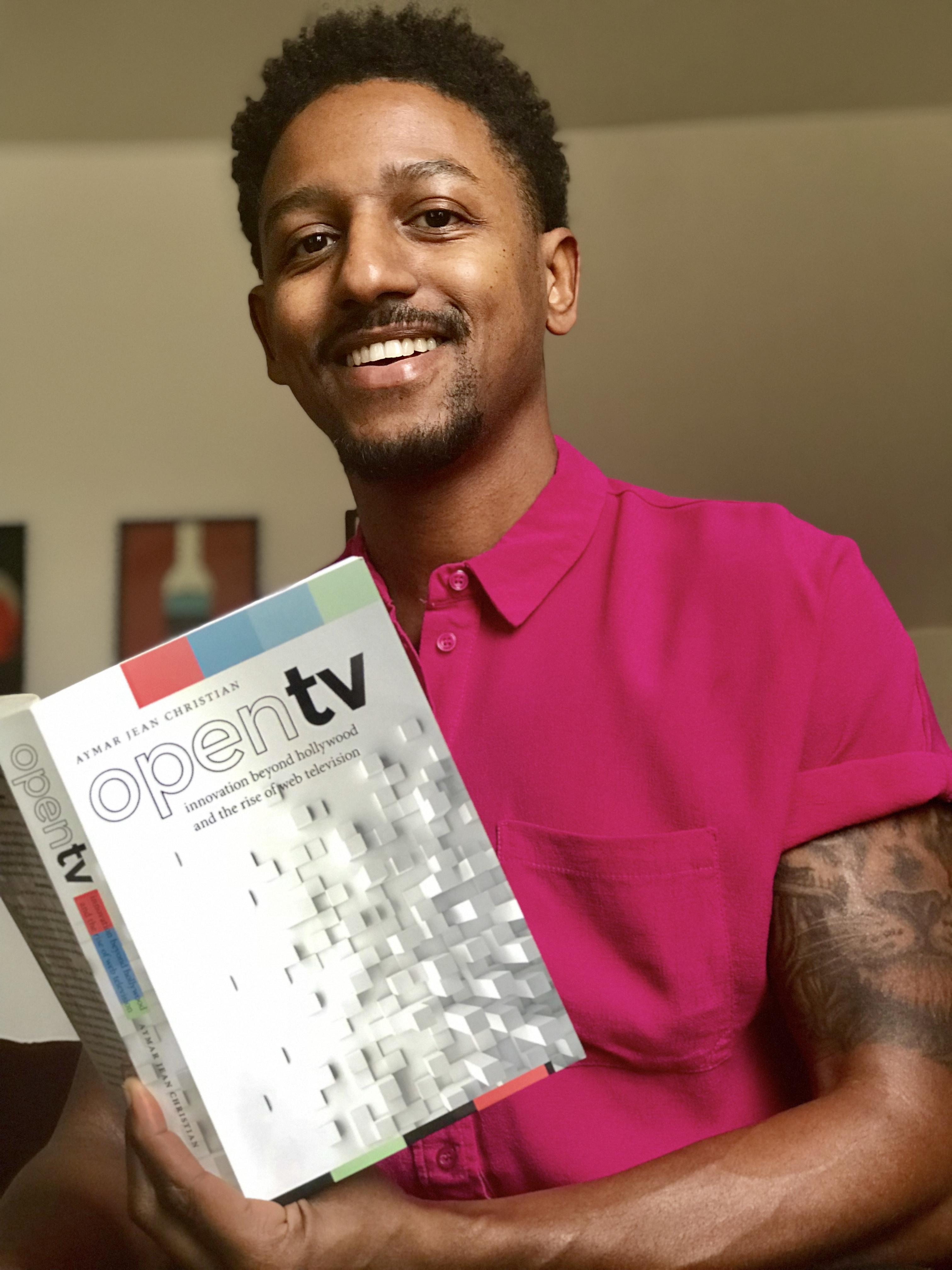 A man smiles while looking up from a book.