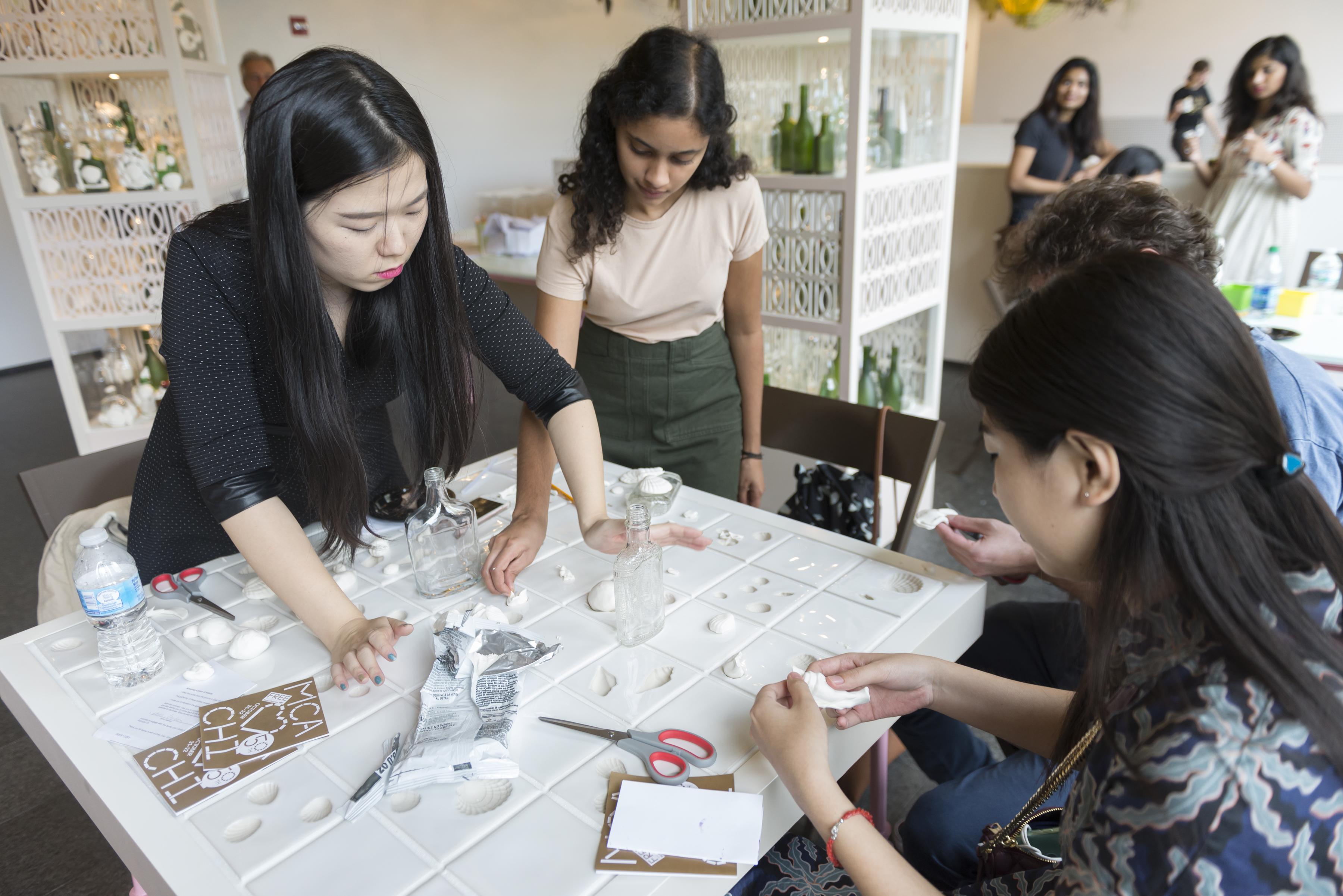 Four people craft seashells by pressing clay into molds on a table.