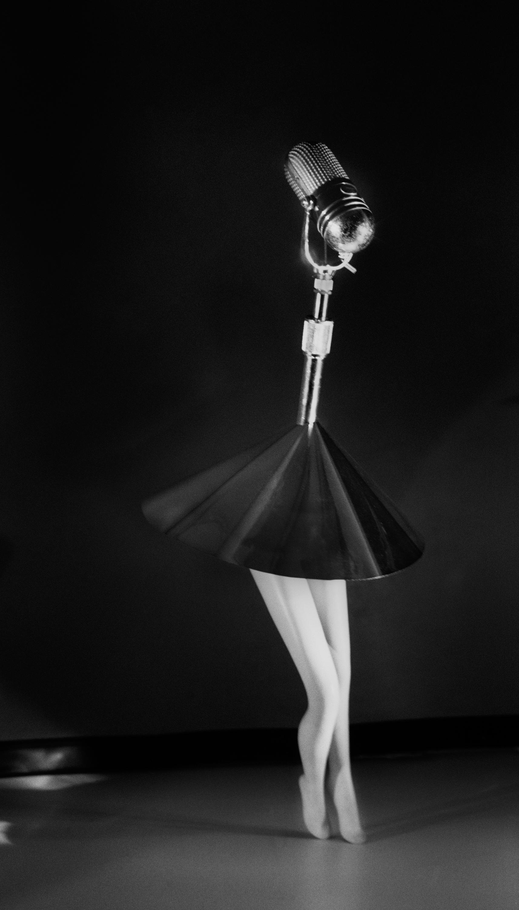 An old-fashioned microphone is mounted atop a short a-line skirt and feminine legs. It appears as though the microphone is performing onstage or posing for a portrait photo.