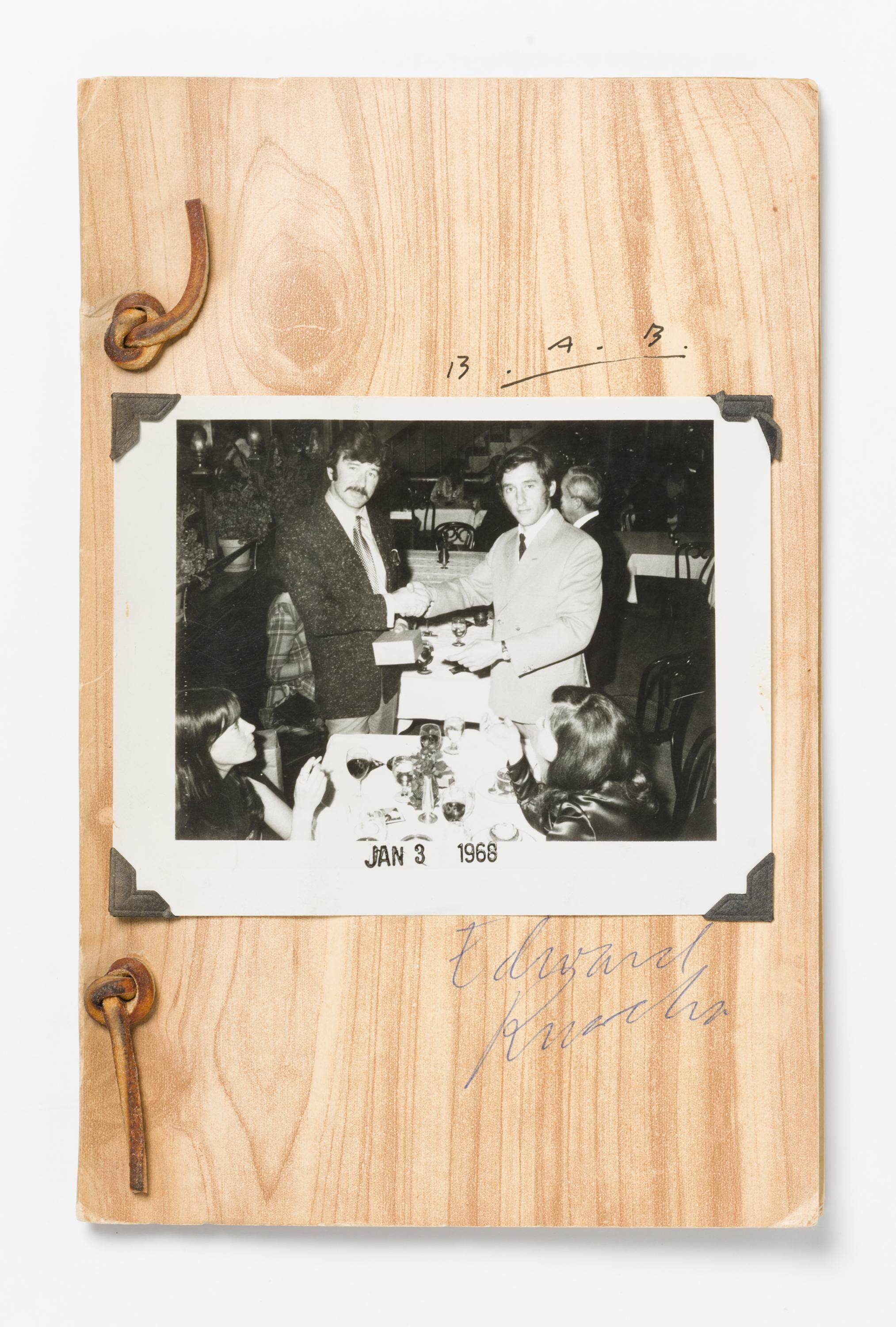 A black-and-white photograph of two men shaking hands is mounted to a light-colored piece of wood.