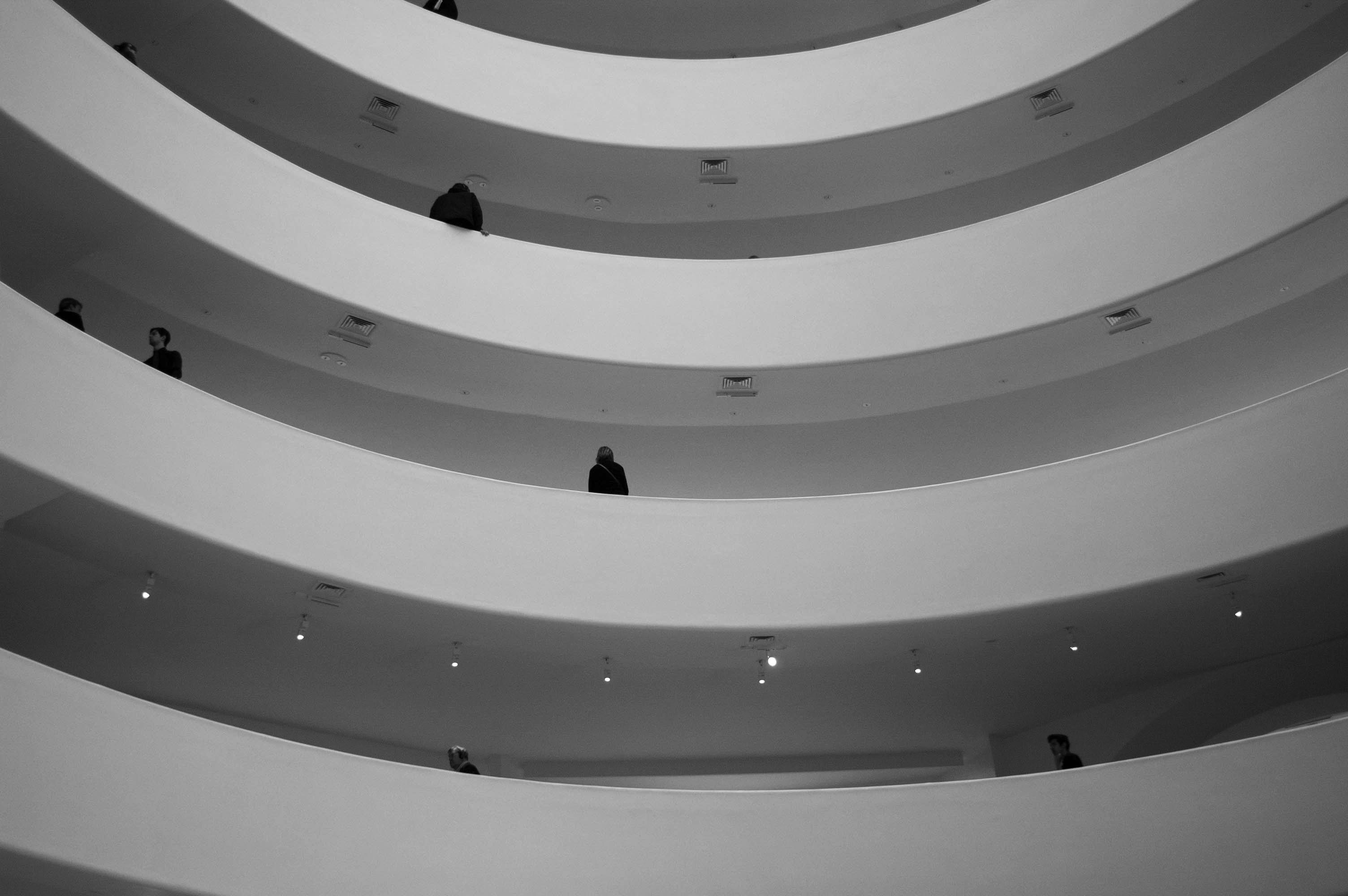 Taken from a lower level looking up, a black-and-white photo shows four levels of a building that curve inwards.