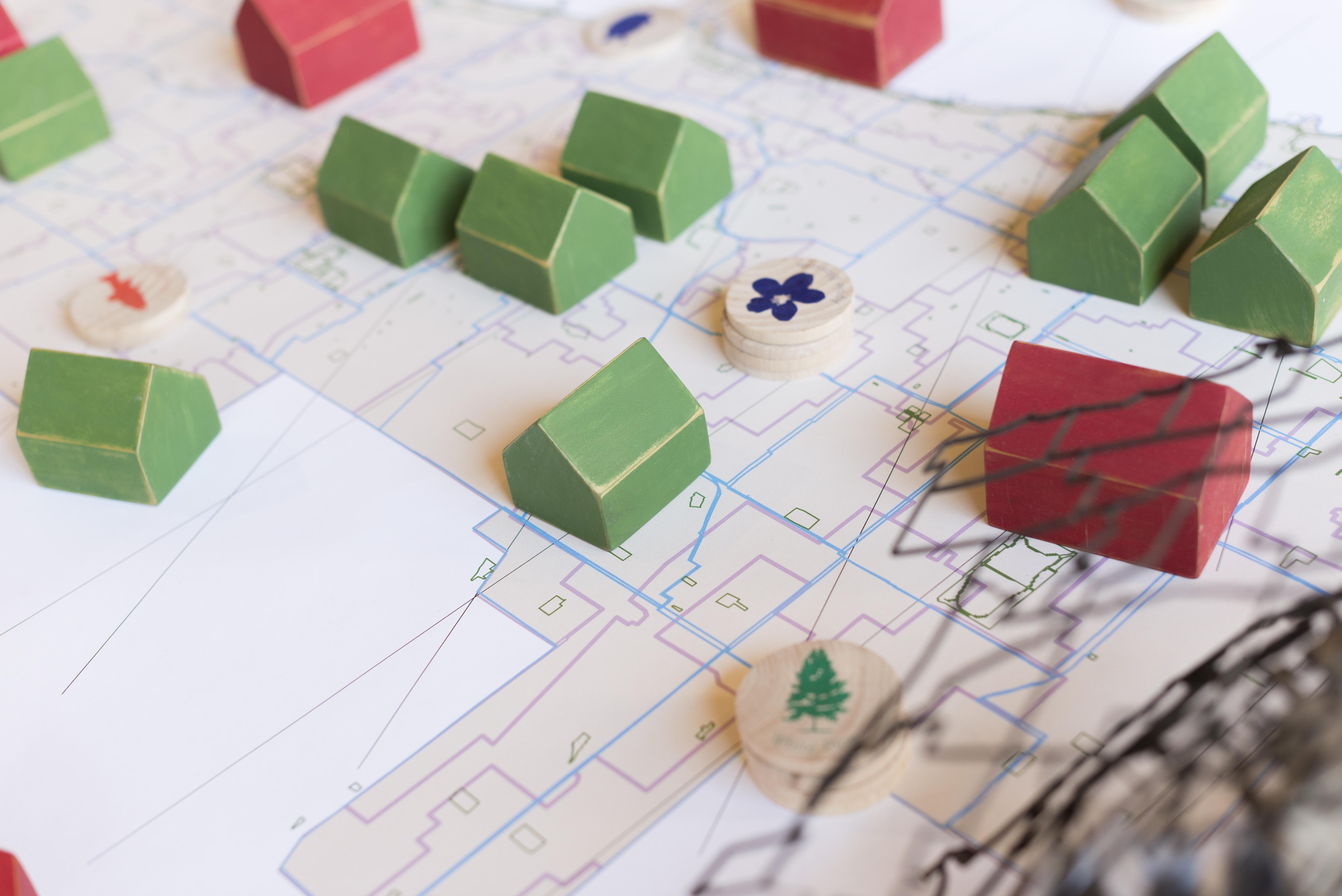 Groupings of small wooden tokens shaped like houses in red and green lay on top of a table with a maplike grid.