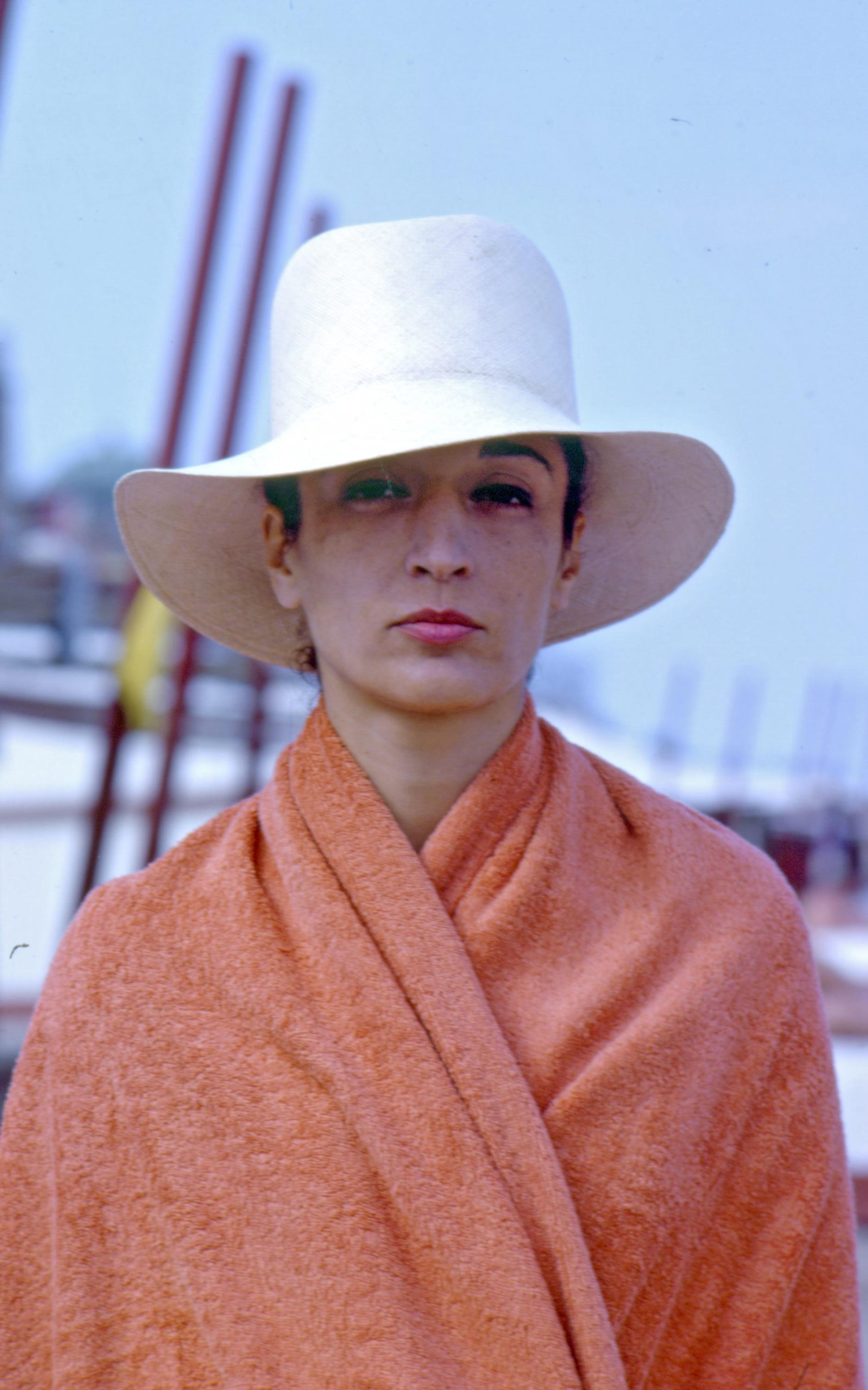 A portrait shows a light-skinned person wearing a large, wide-brimmed white hat and an orange shawl or blanket.