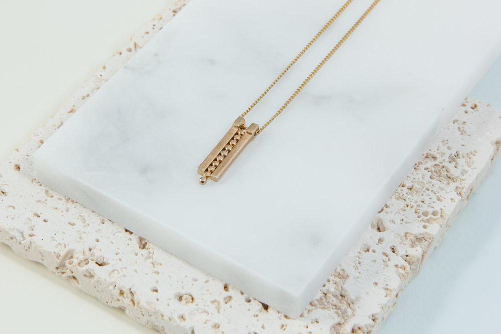A delicate geometric gold necklace rests on a marble display.