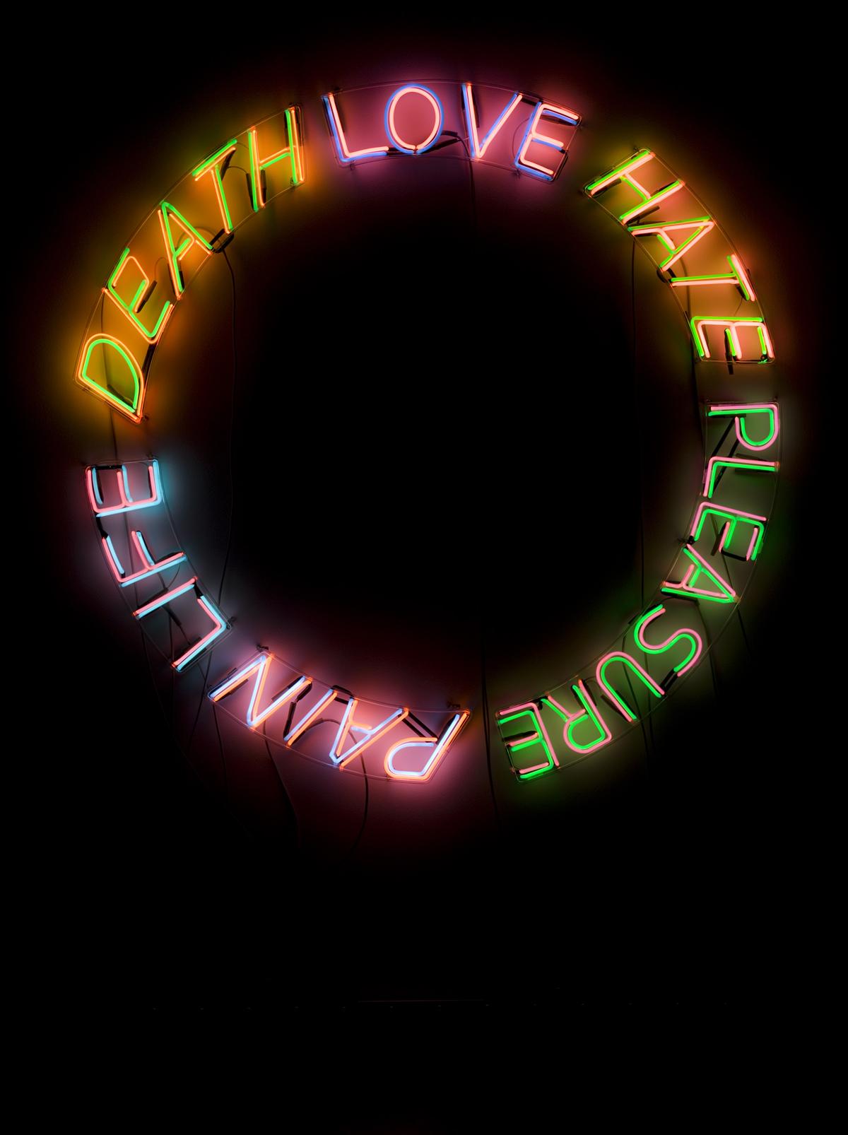 The words "DEATH," "LOVE," "HATE," "PLEASURE," "PAIN," and "LIFE" appear in illuminated neon, organized in a circle against a black background. In order, their colors are orange, purple, pink, green, and blue.