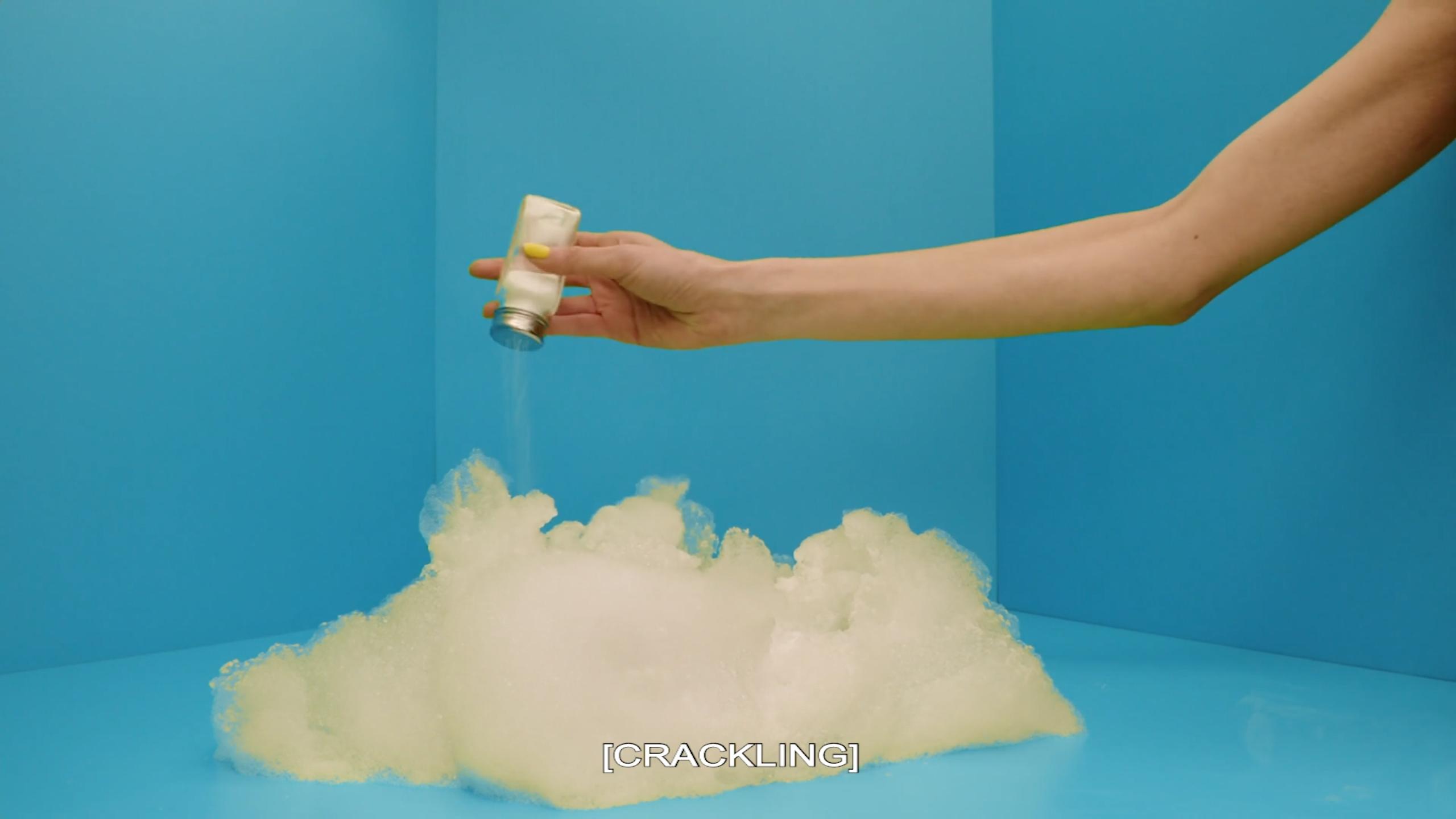 An arm extends into a blue room, shaking salt onto a cloud-like mass. Text on the image says [CRACKLING].