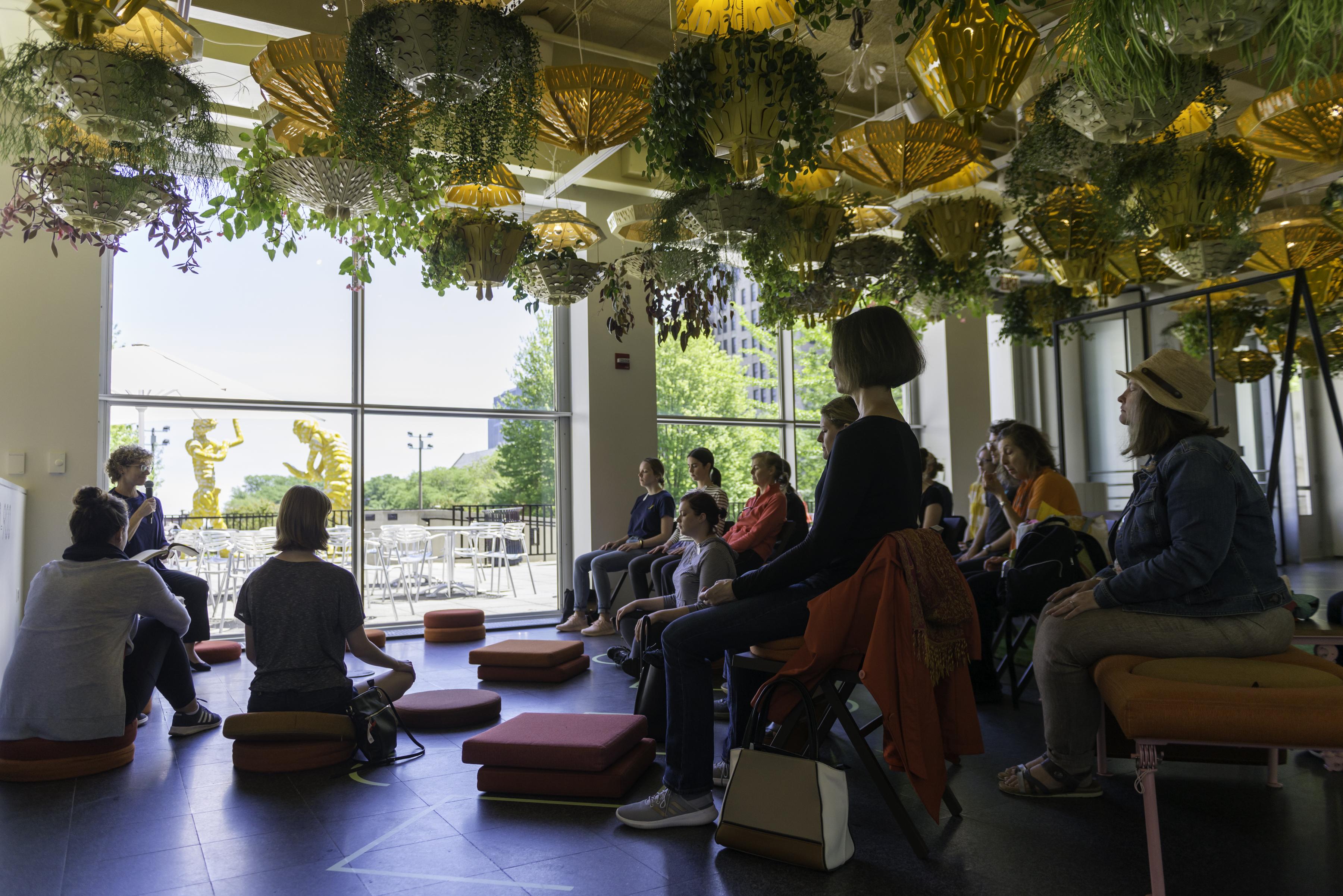 A group of people sit in meditation beneath the ceiling planters of the Commons.