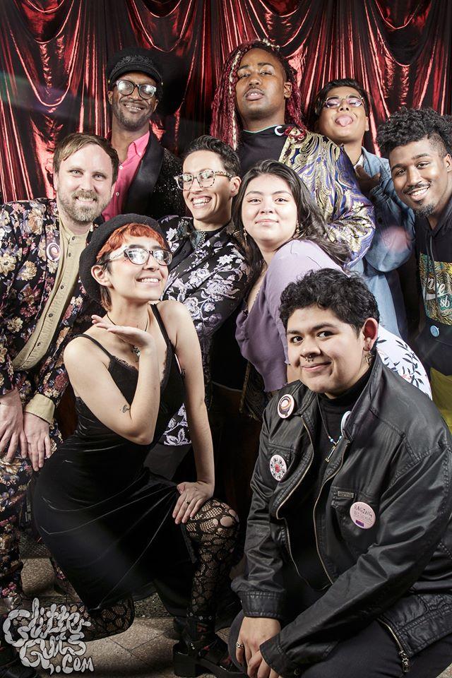 A group of nine young people pose for a group photo in front of a red satin curtain.