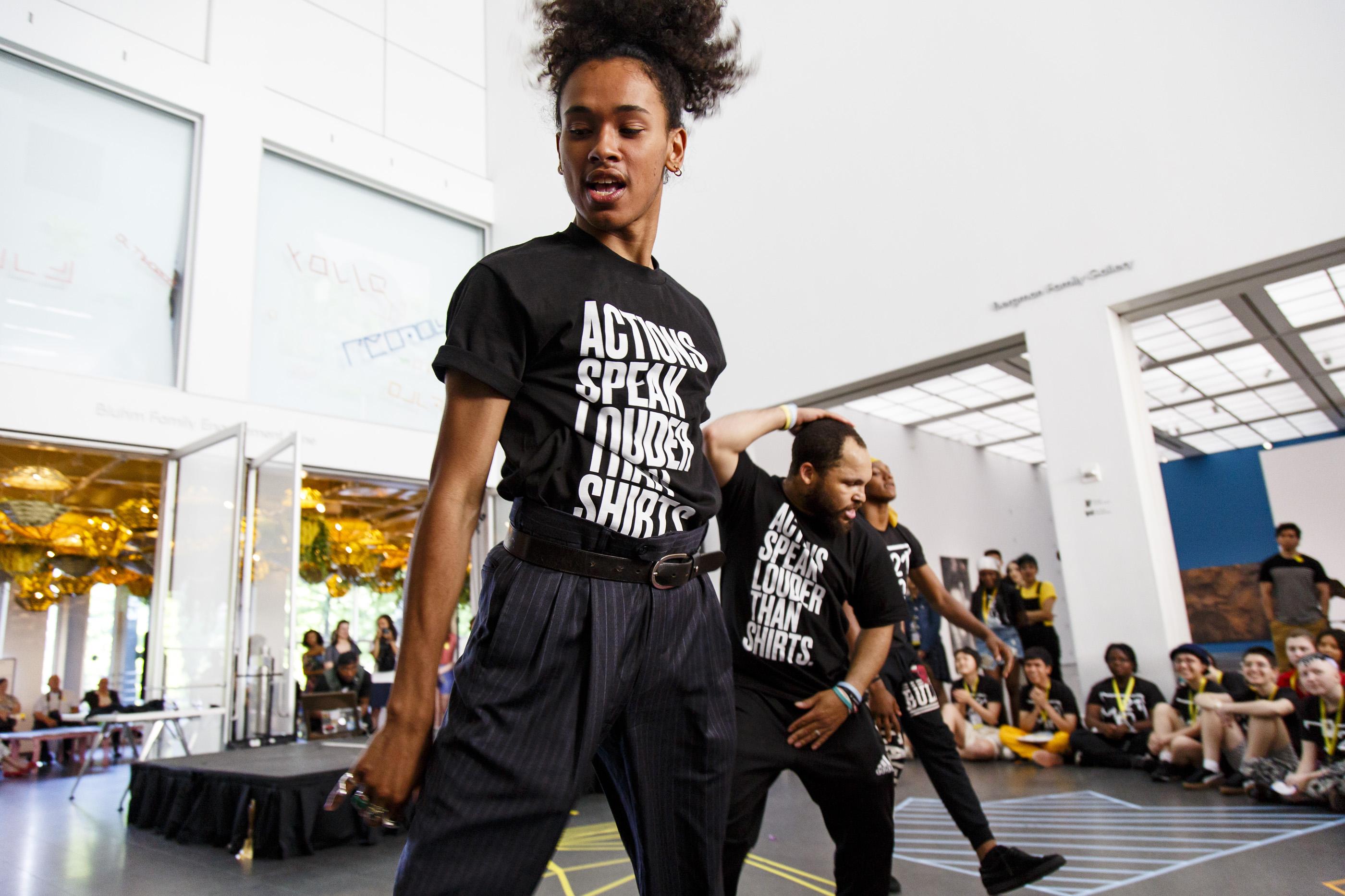 Three dancers perform in the MCA Atrium as dozens of audience members watch.