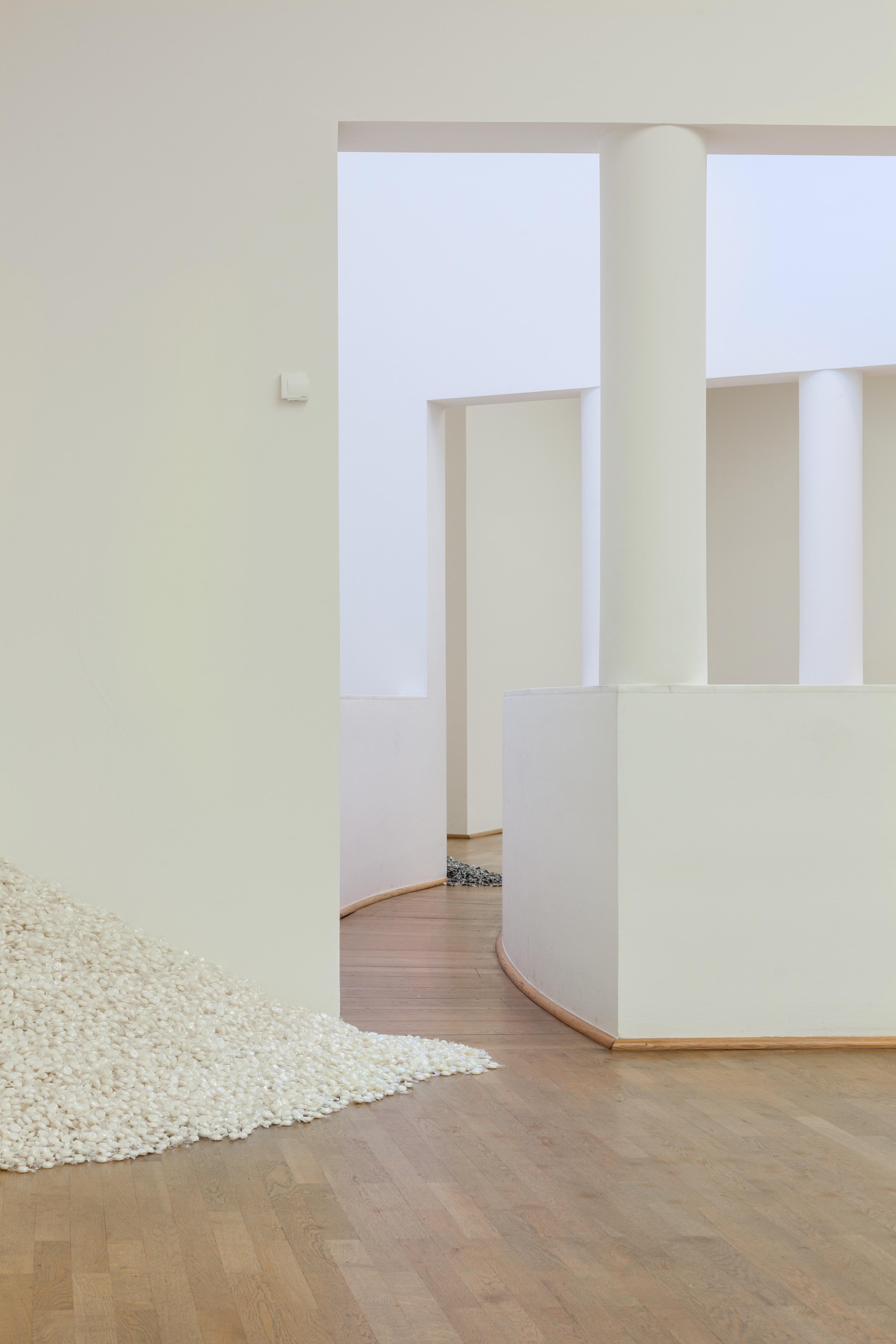 A gallery space with views into three somewhat empty rooms. On the floor of the first room is a large pile of white candy.