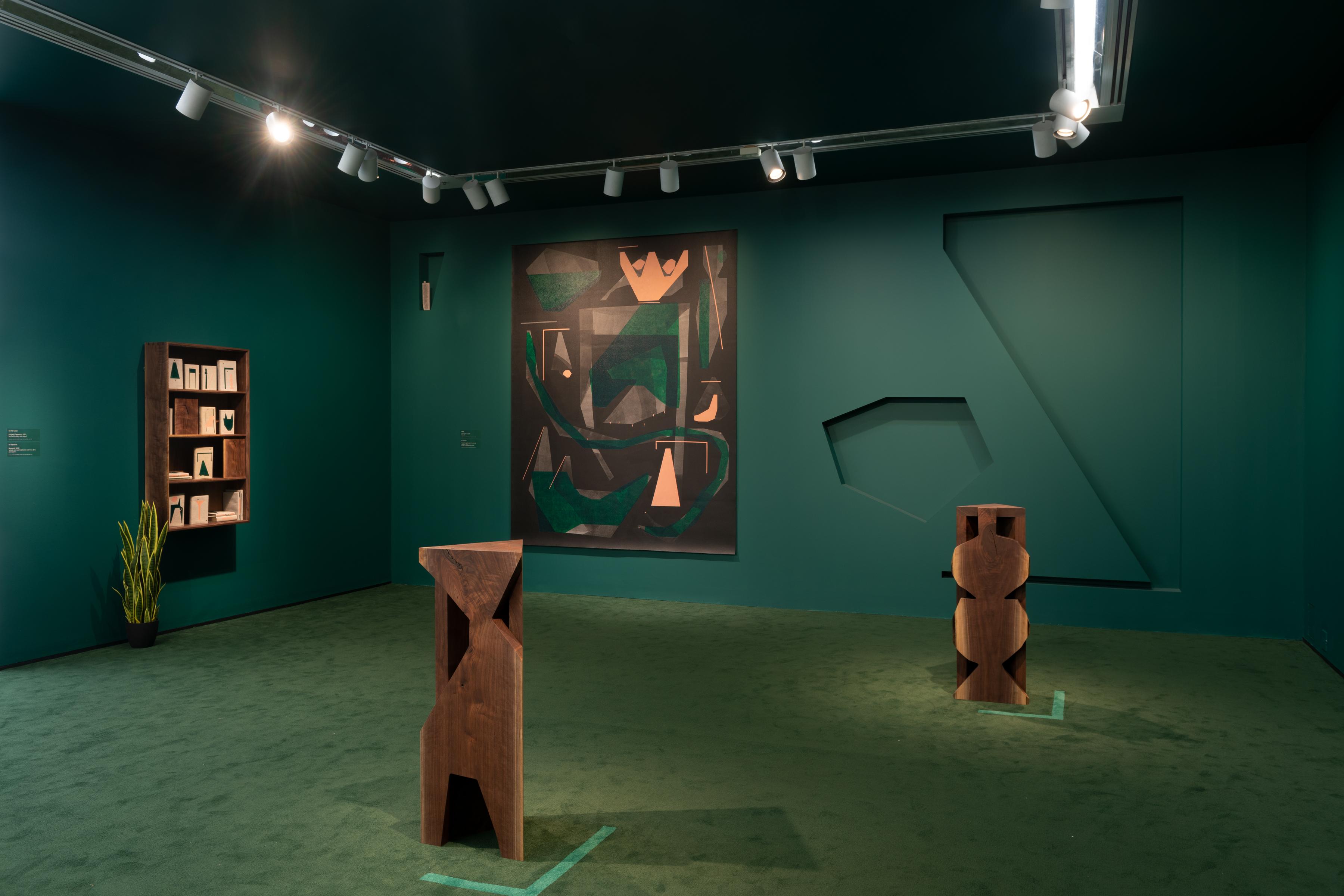 Corner of a room with dark green walls, a painting, and 2 wooden carved plinths