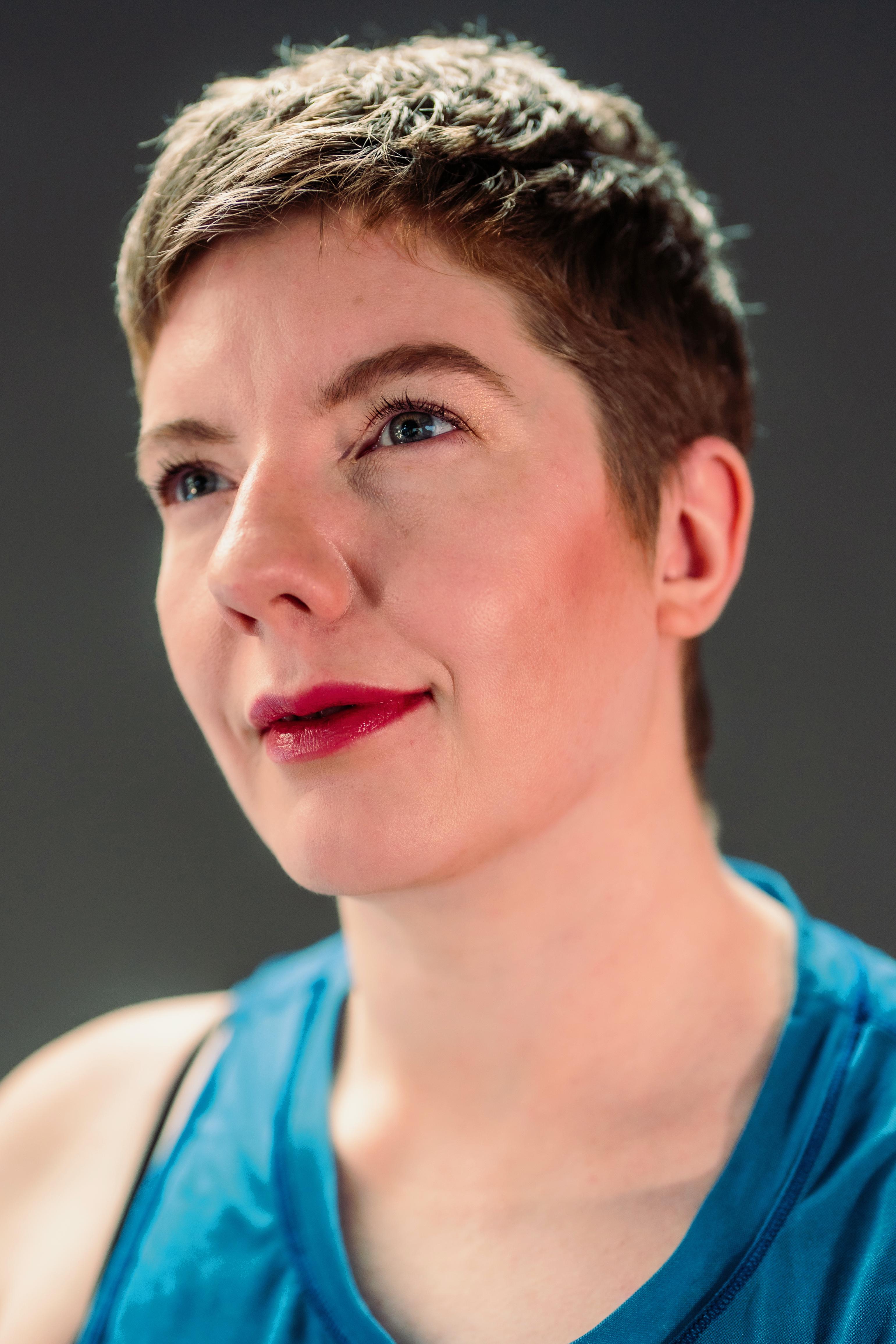 Laurel Lawson headshot. She is a white woman with short-cropped brown hair. Her chin is lifted and her gaze directed upwards with a slight smile; her blue eyes compliment her blue tank top.