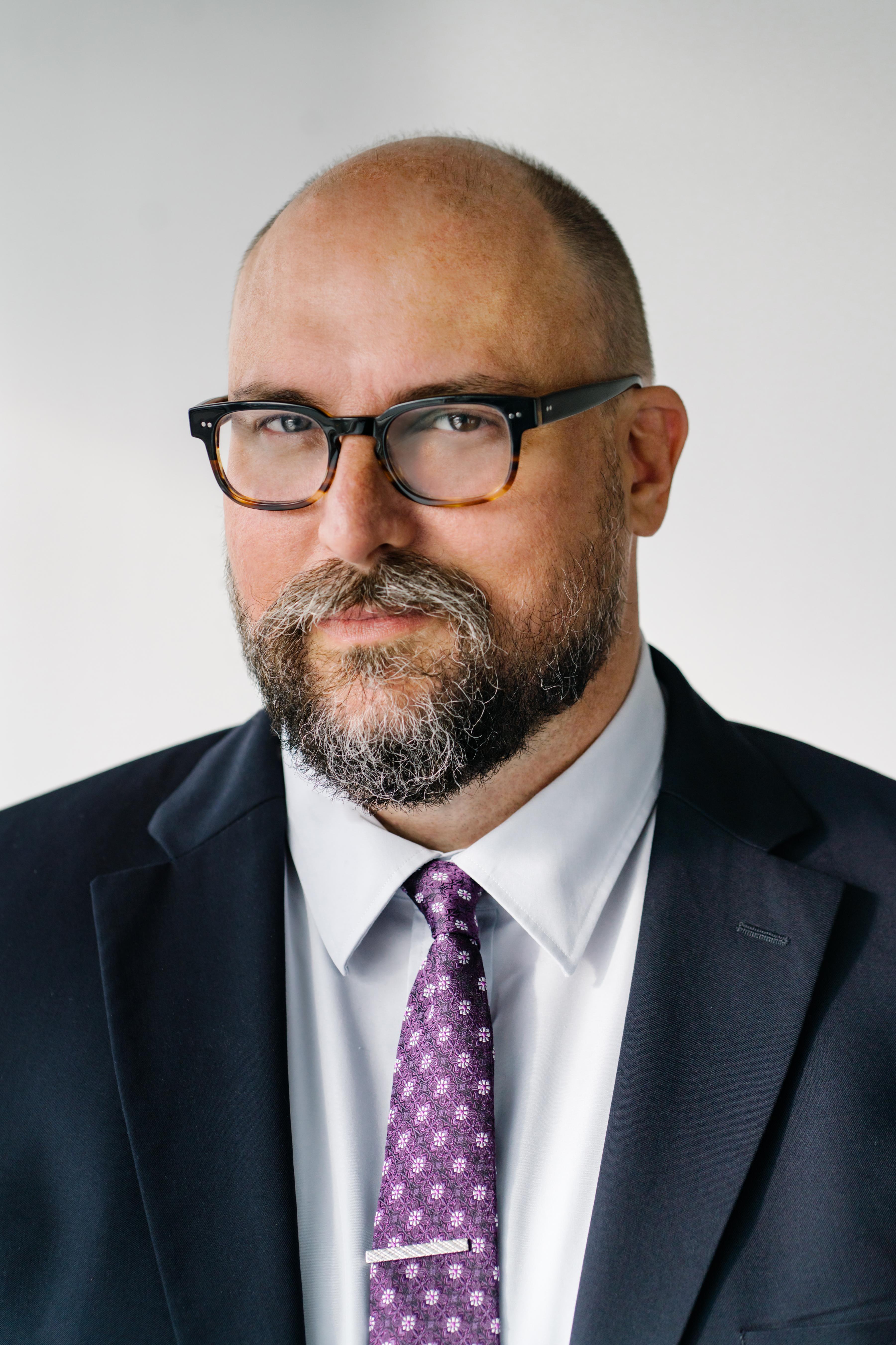 Headshot of a man wearing a suit and glasses