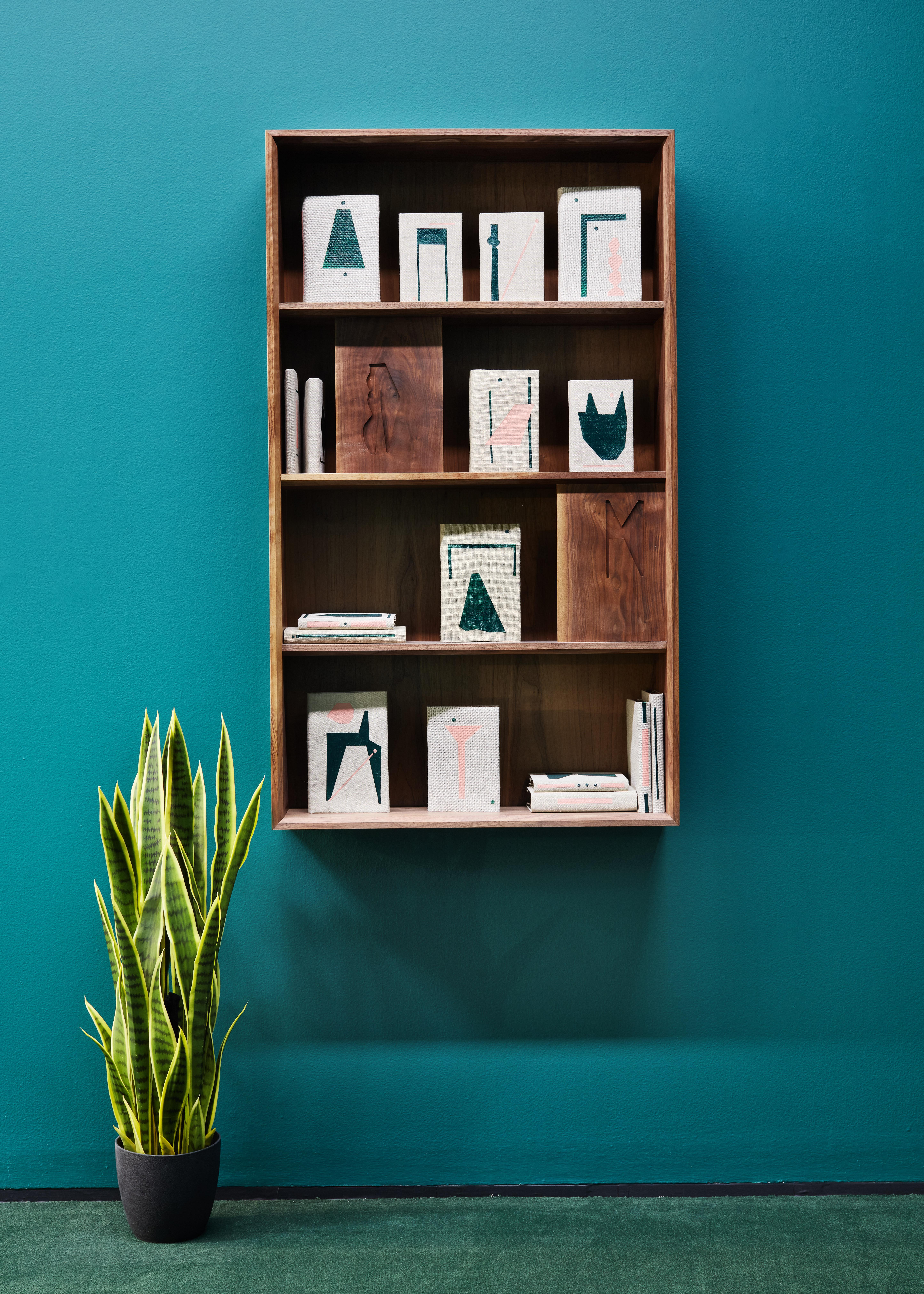 A wooden bookshelf hangs on a dark green wall next to a potted plant