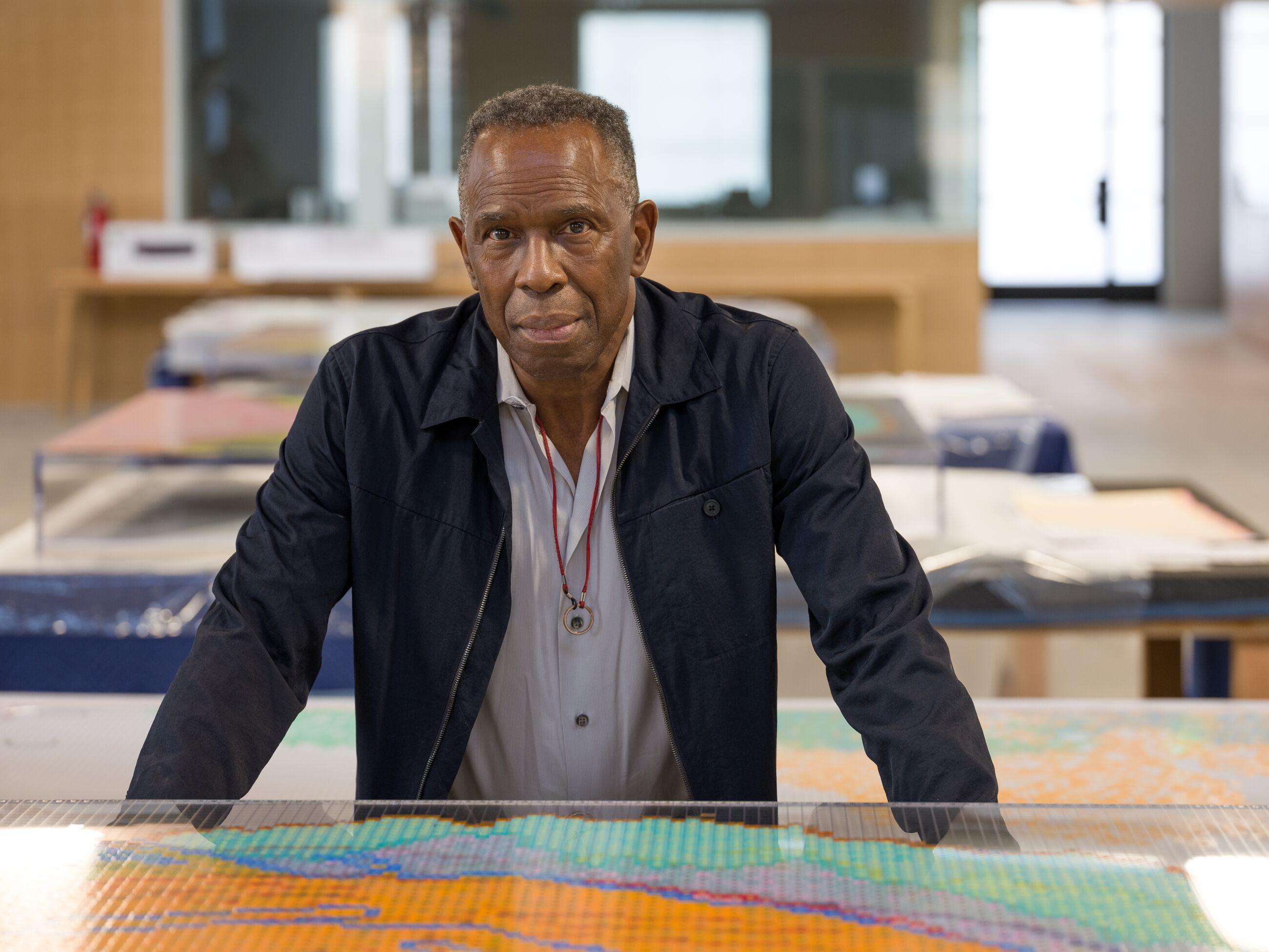 Charles Gaines stands leaning forward against a display case