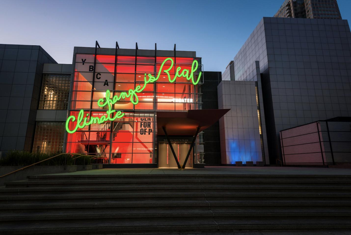 exterior of building with large neon cursive handwriting with the text 'climate change is real'