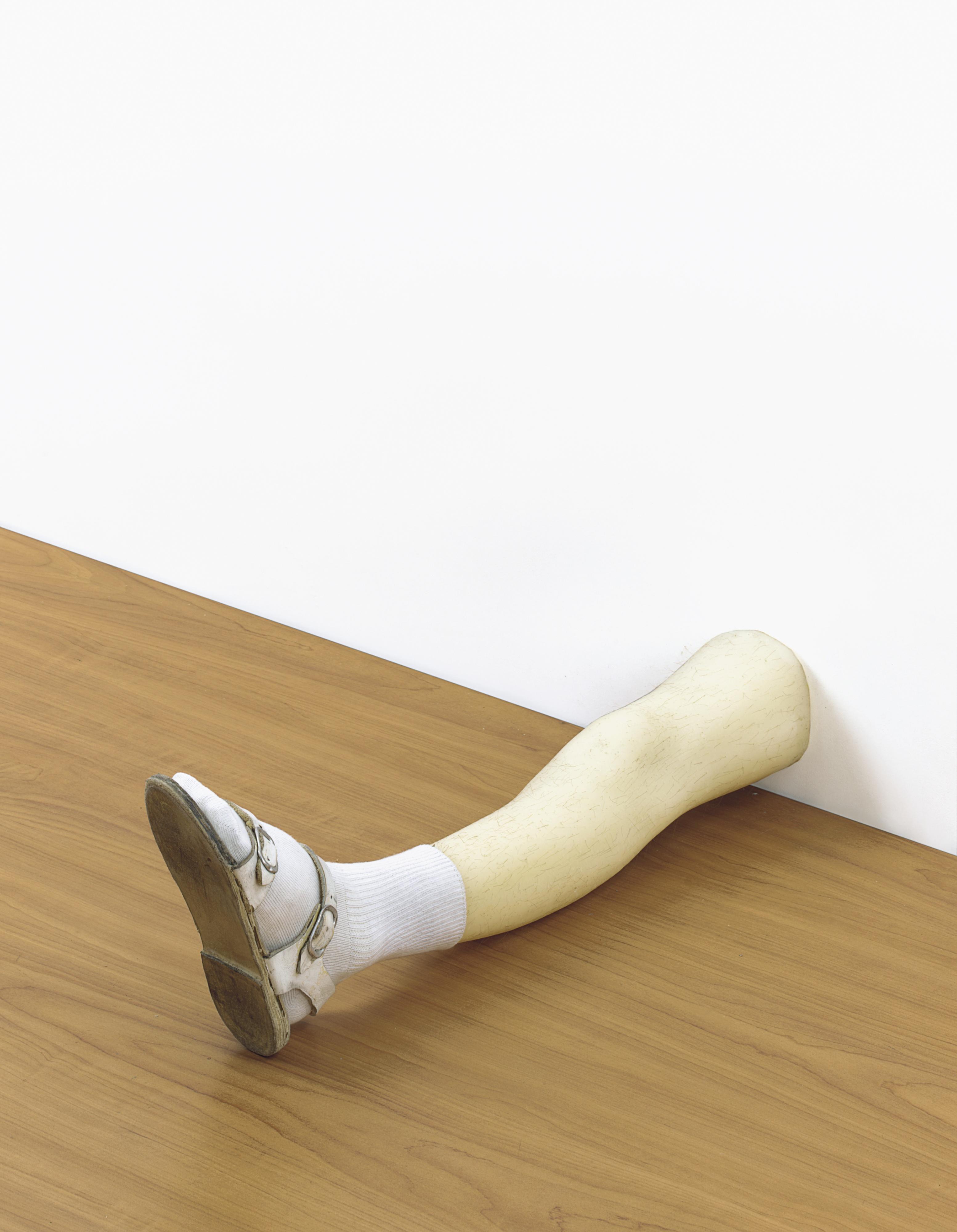 sculpture of a leg protrudes from a gallery wall