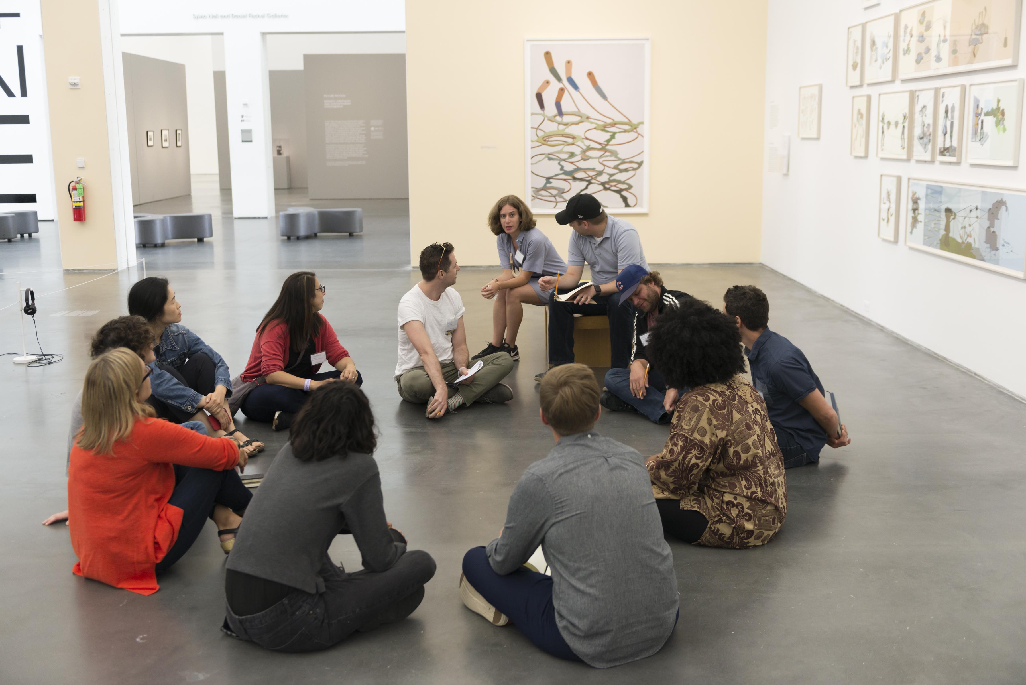 A group circled sitting on floor in gallery space