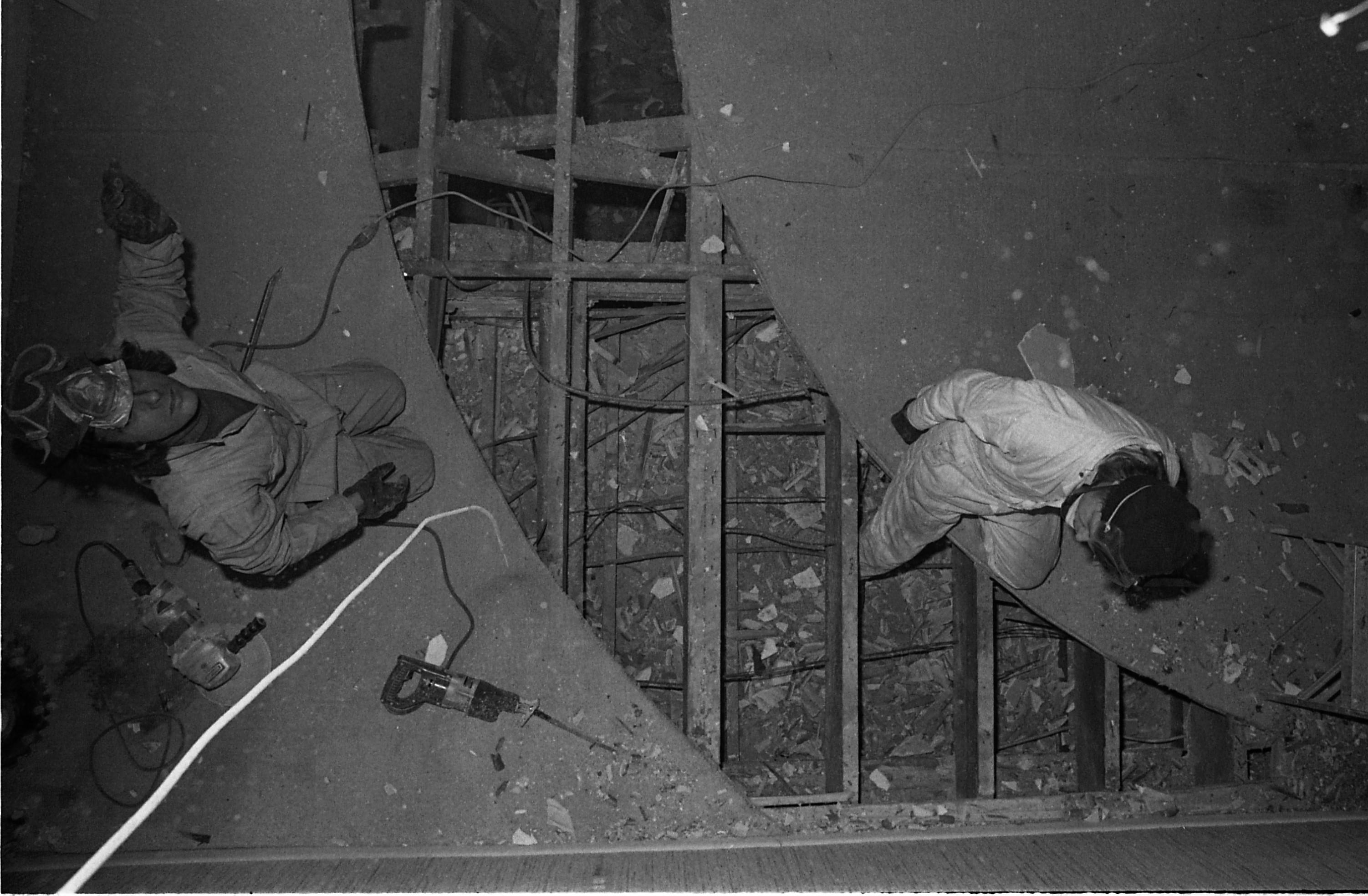 Two people in coveralls sit on the edge of a curved cut in a floor.