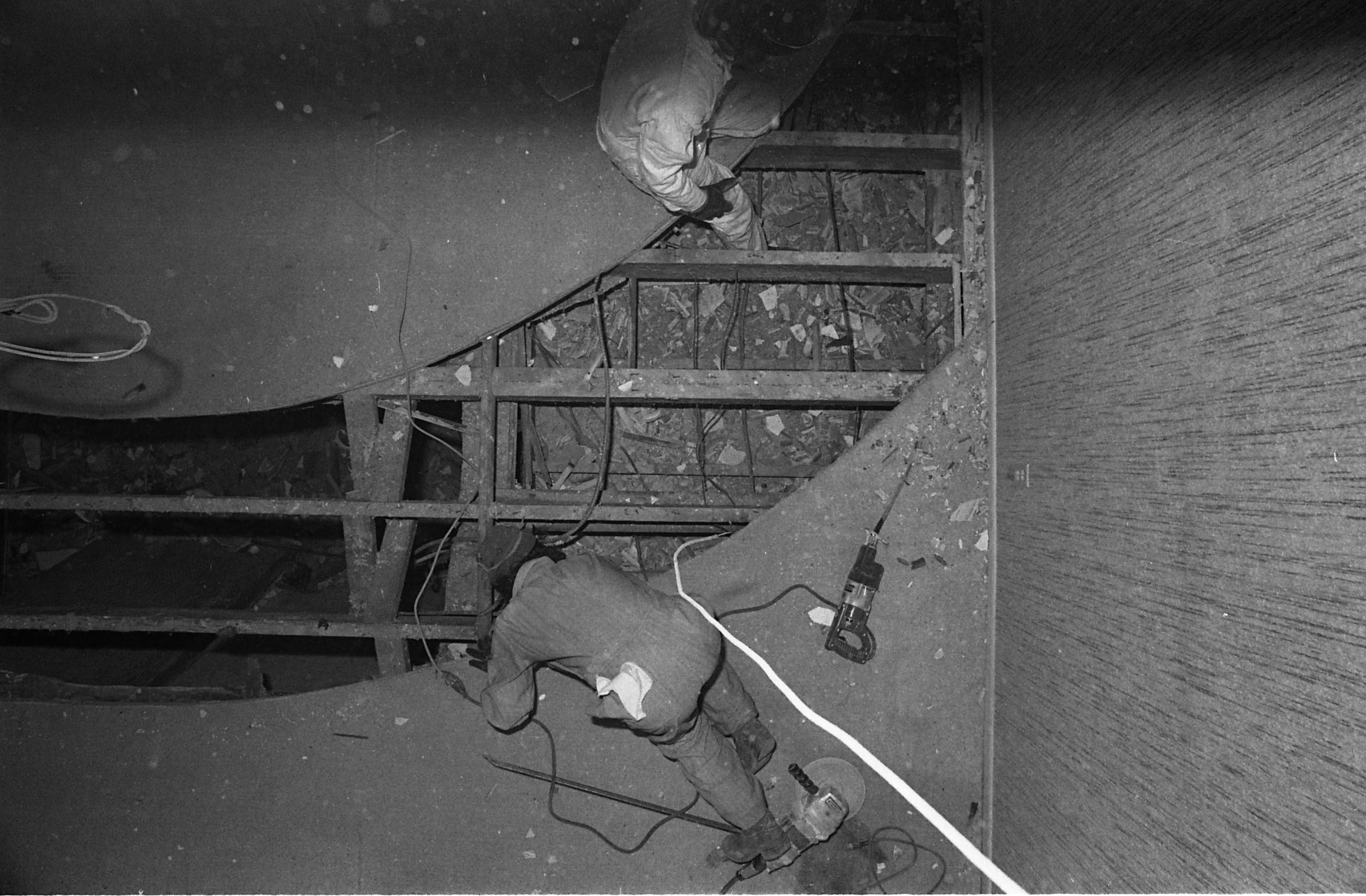 A person in coveralls lays on the ground looking down through a large cut away portion of the building.