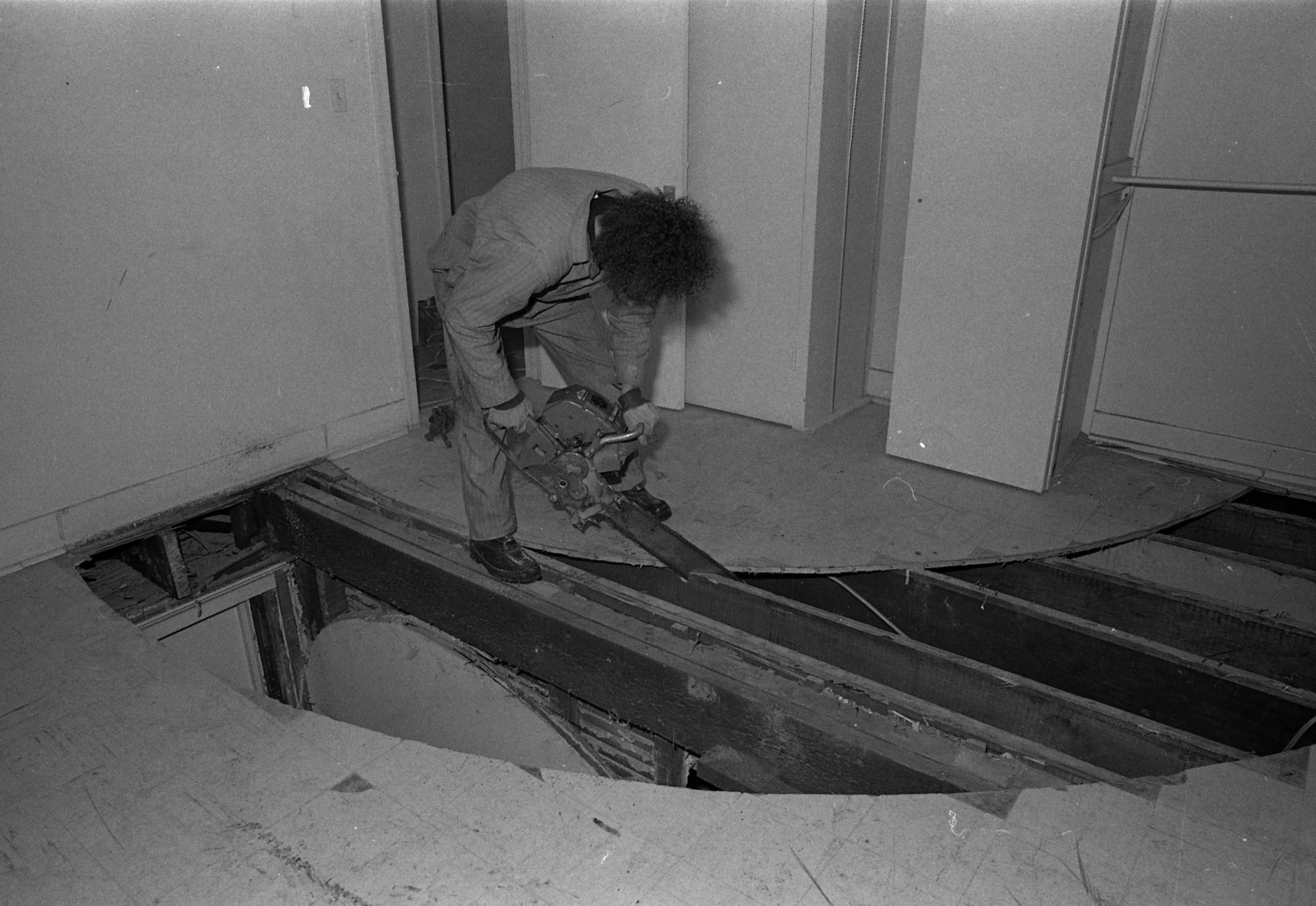 A person uses a chainsaw to cut through floorboards.