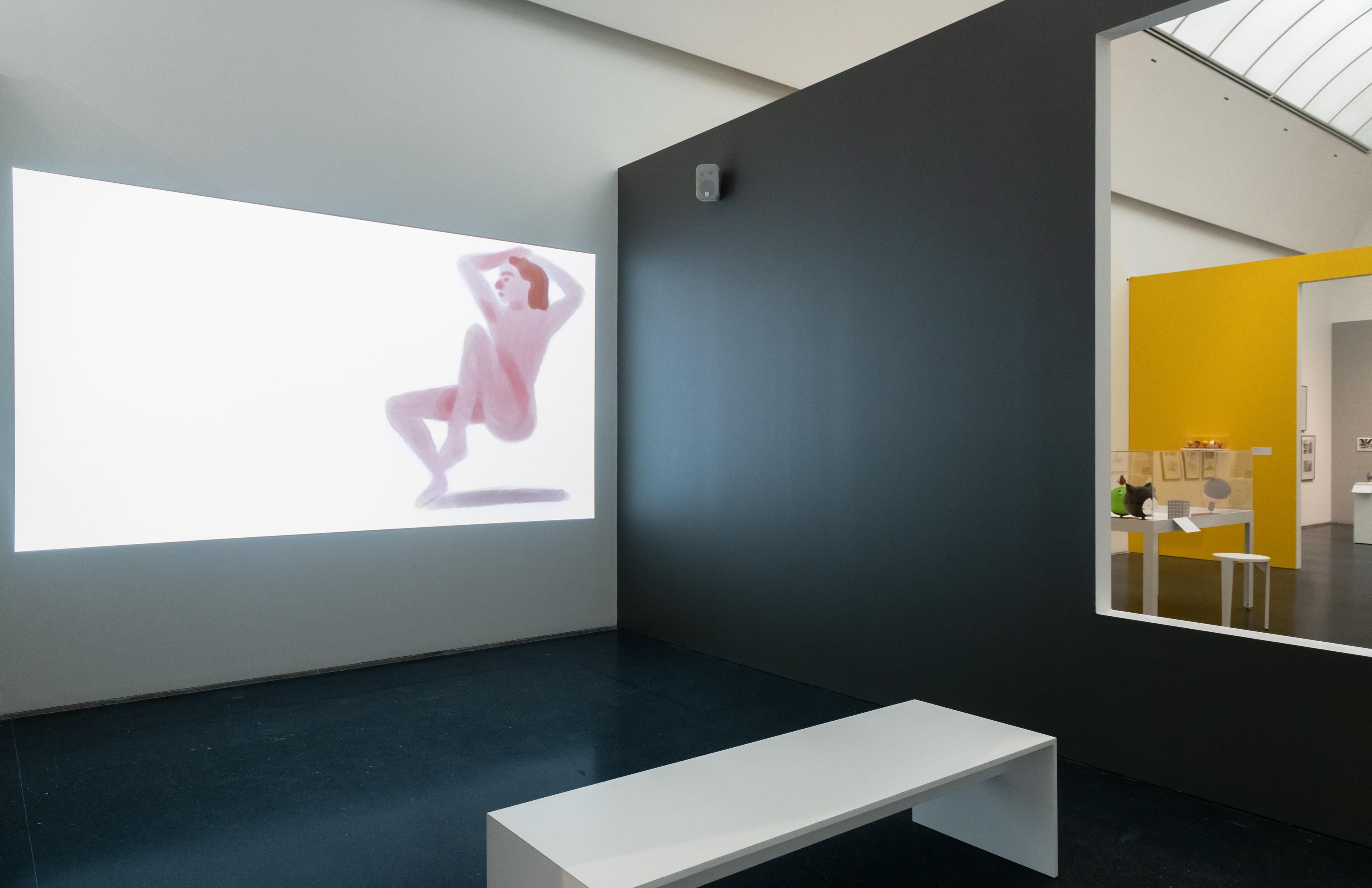 A still of a seemingly nude illustrated person in a lounge position is projected on a wall.
