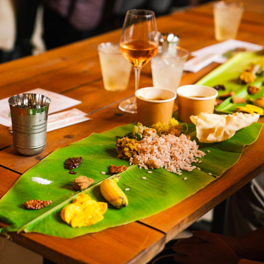 A banana leaf laid out on a wooden table covered with a variety of foods.