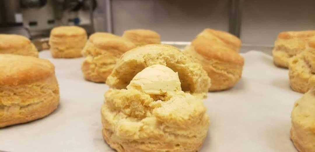 Ten baked biscuits scattered around a baking tray on parchment paper. The middle one closest to the foreground is broken open and has a large pat of butter in it.