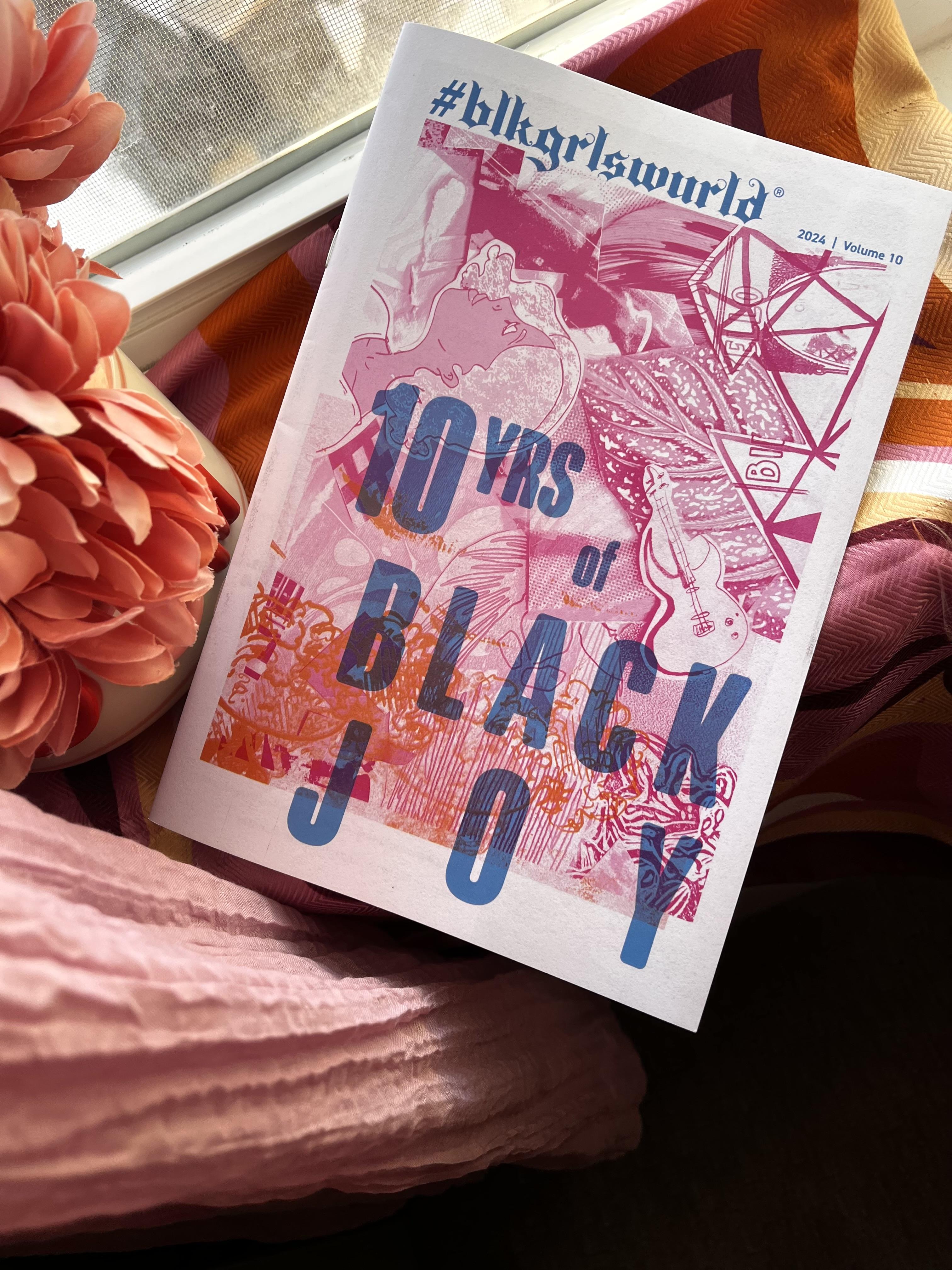 blkgrlswurld zine titled 10 yrs of Black Joy displayed on top of pink and salmon colored pillows near a window