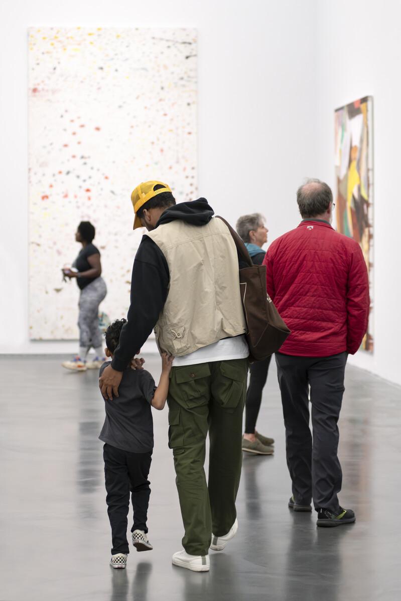 A group of people of various ages in a gallery with large paintings hung on the walls.