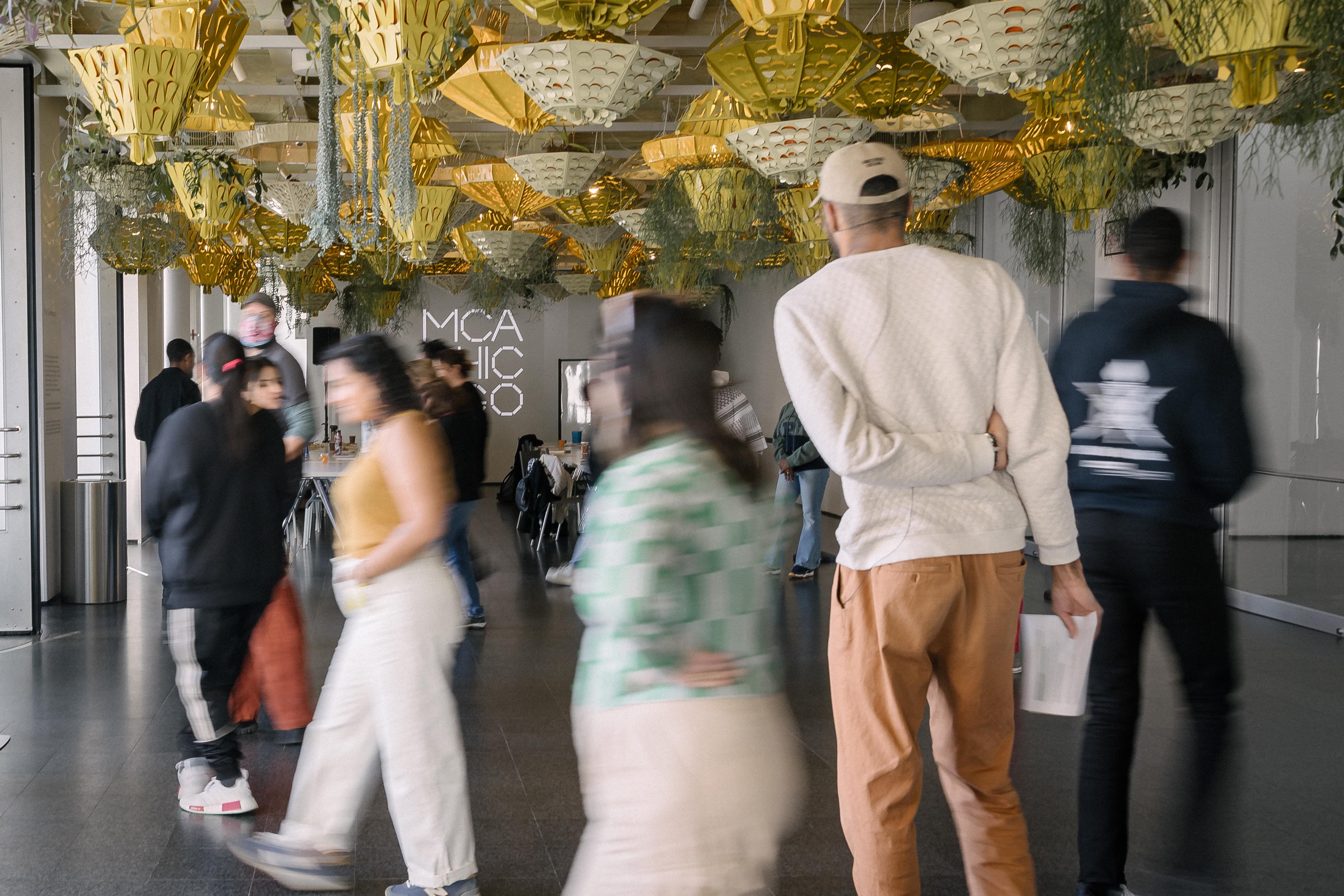 A long exposure photo of people moving through a room filled with many lights and plants hanging from the ceiling