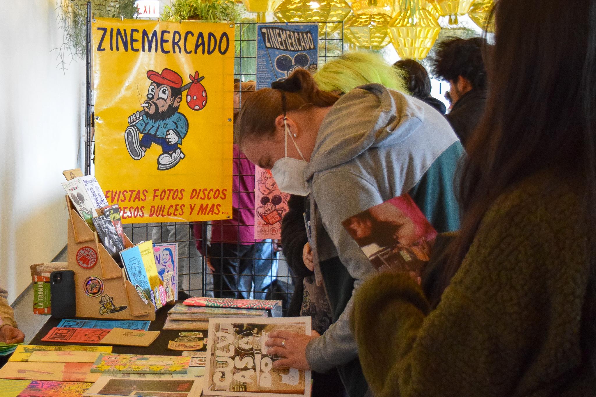 People look at zines at a table featuring a poster headed "zine mercado"